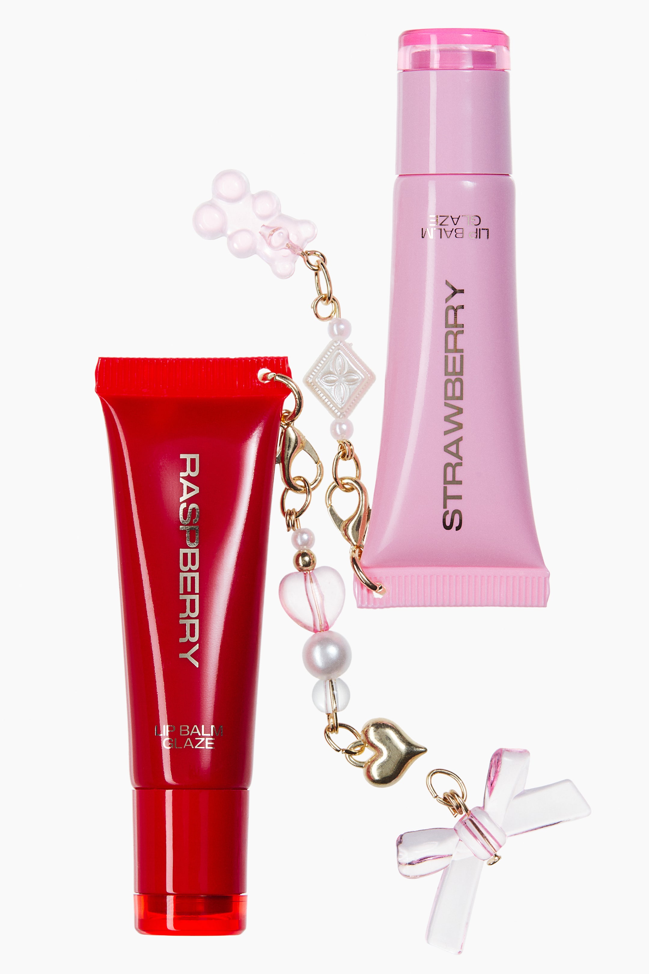 Größeres Bild anzeigen: Ein Lip Balm Glaze Duo zeigt eine rote Tube mit der Aufschrift „RASPBERRY“, die aufrecht steht, und eine hellrosa Tube mit der Aufschrift „STRAWBERRY“, die kopfüber liegt, beide nach vorne ausgerichtet. Die Tuben sind über goldfarbene Ketten mit Karabinerverschlüssen verbunden, an denen dekorative Anhänger zu sehen sind, darunter ein rosa Gummibärchen, ein goldenes Herz, Perlen und eine transparente Schleife.