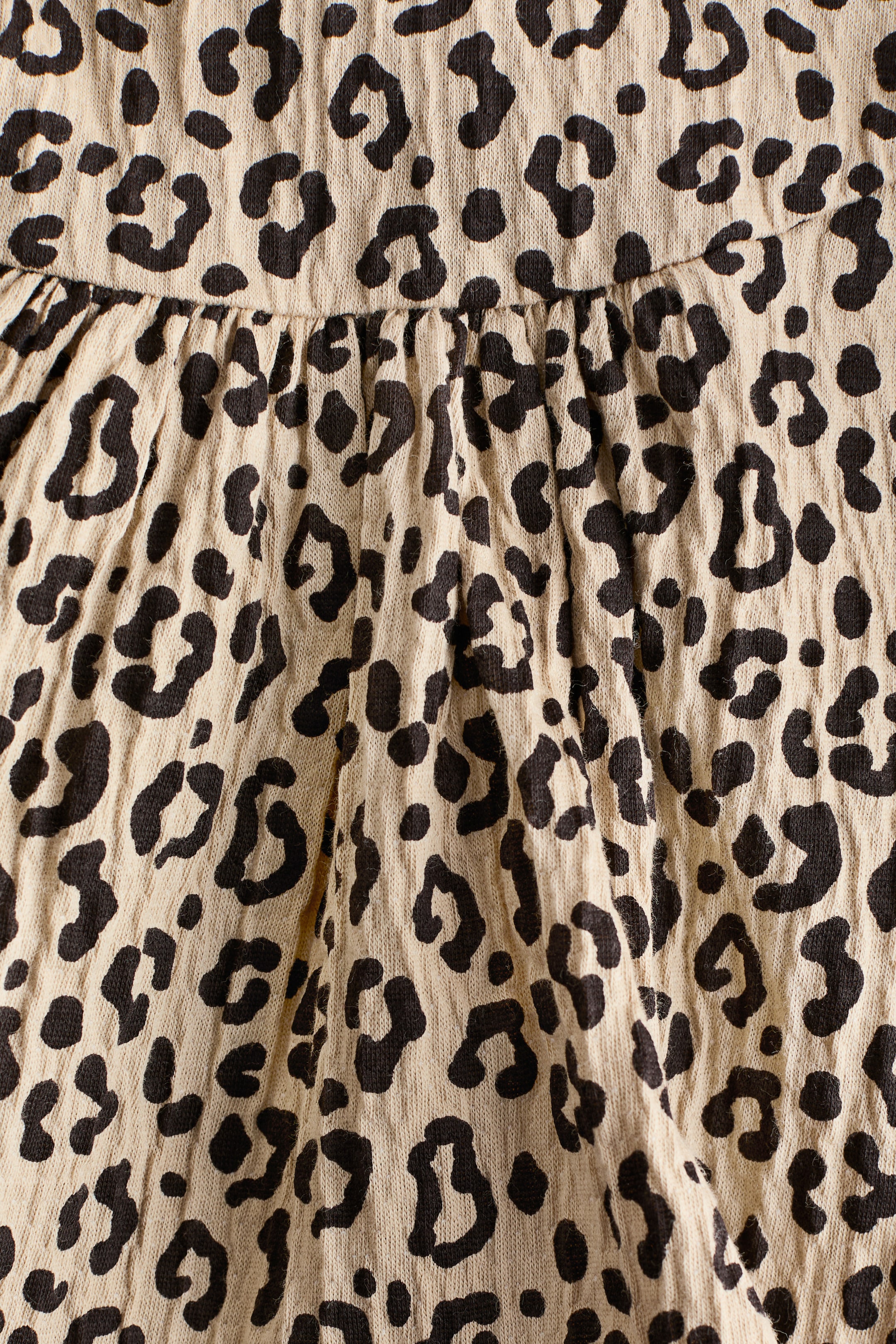 Ver imagem maior: Uma blusa em jersey frisado, em tecido bege com estampa de leopardo preta, apresenta uma costura na cintura na FRENTE, com franzidos abaixo dela para maior volume.