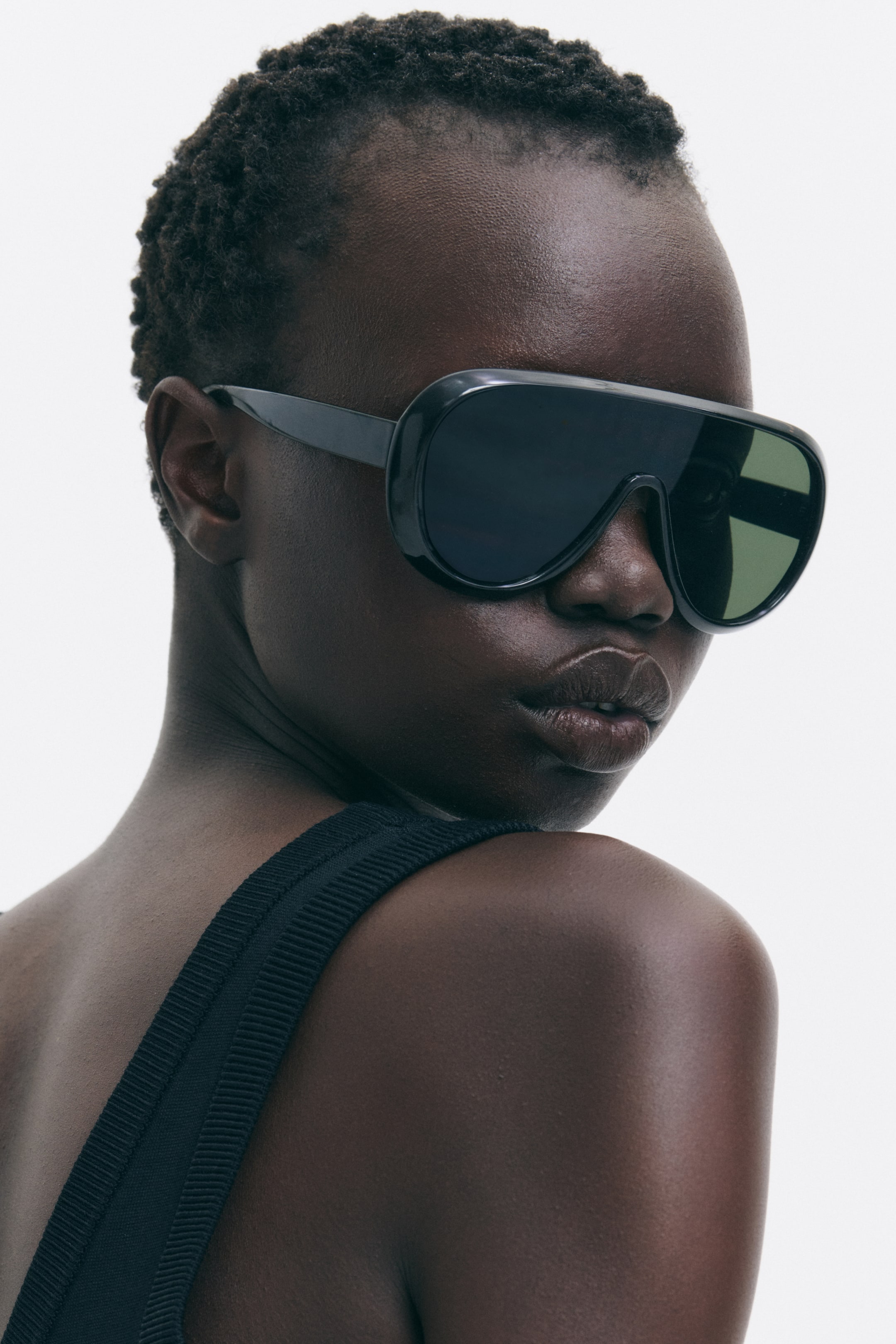 View larger image: The model is wearing shield sunglasses featuring black plastic frames and sidepieces, along with dark, tinted, UV-protective plastic lenses.