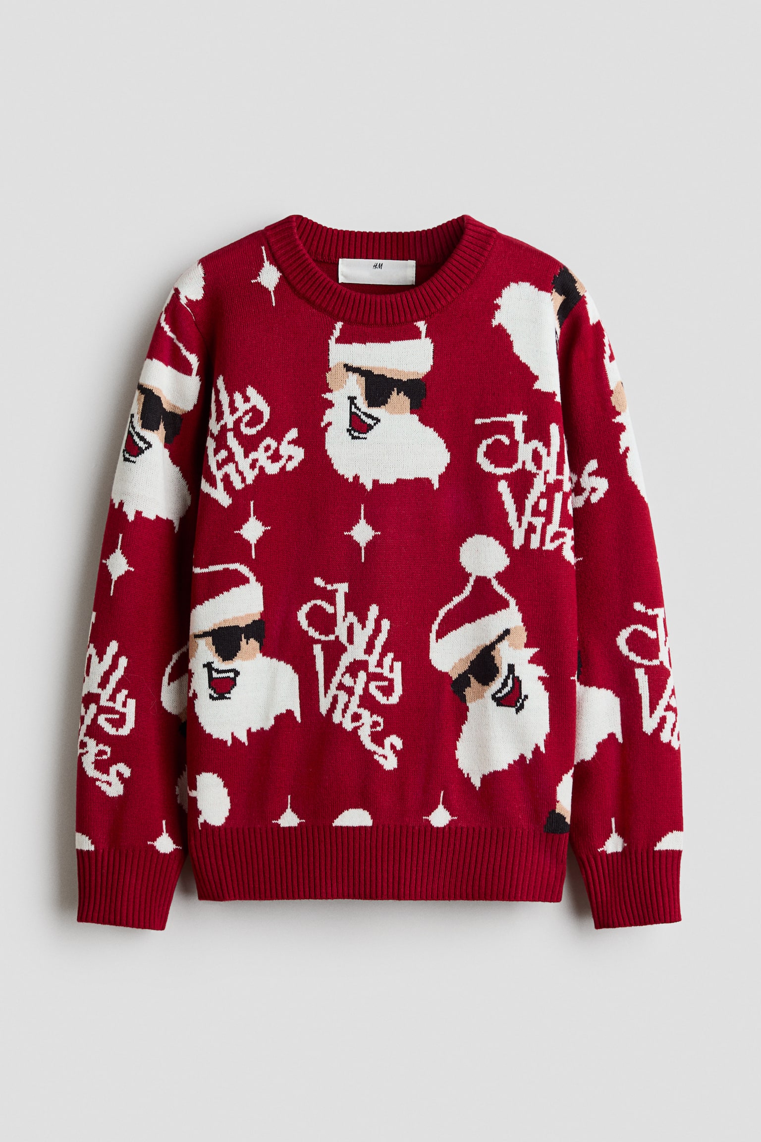 En rÃ¸d sweater med lange Ã¦rmer og rund hals er vist forfra og har et gentaget strikkemÃ¸nster med Julemanden ifÃ¸rt solbriller, stiliseret hvid skrivetekst med ordene "Jolly Vibes" samt smÃ¥ hvide stjernemotiver. Plagget fremviser en ribstrikket halsudskÃ¦ring, ribstrikkede manchetter og en ribstrikket kant.