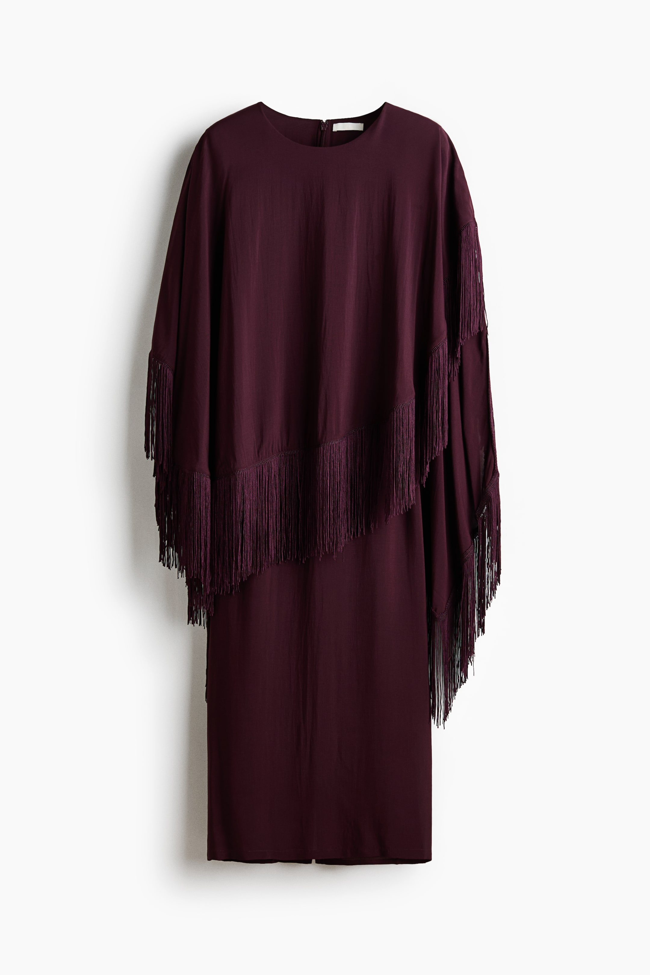 View larger image: A dark burgundy midi dress is hanging front-facing, featuring a round neckline and an asymmetrical cape-style overlay with long fringe trim draping over the shoulders and bodice.