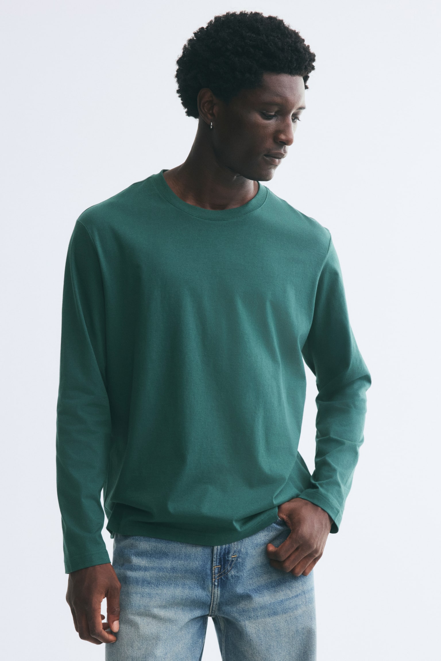The model is wearing a green long-sleeve top in a regular fit, featuring a round rib-trimmed neckline and a straight hem. The top is styled with light-wash blue jeans. - 1