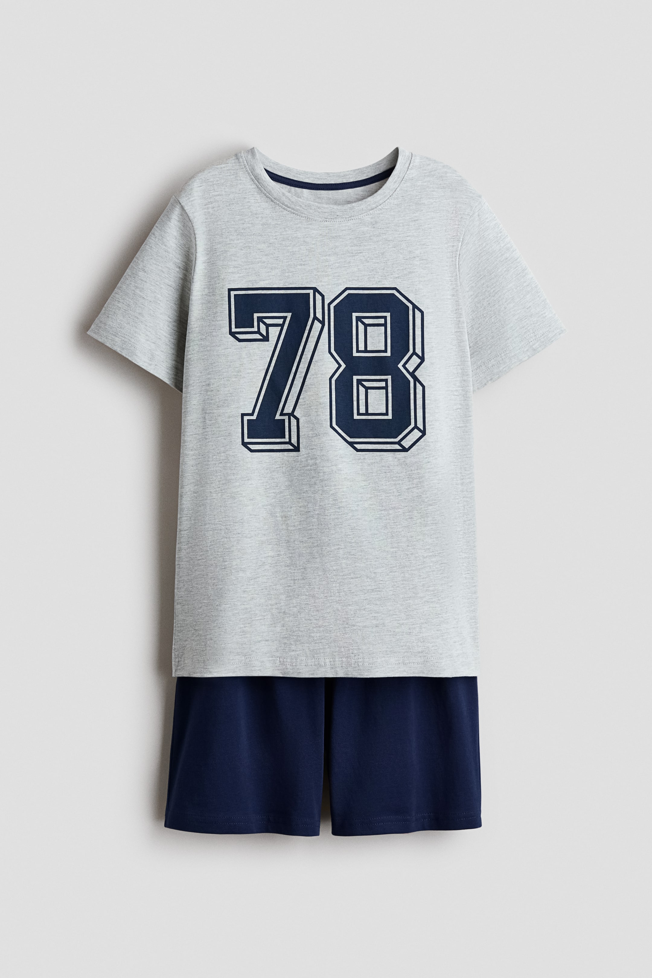 View larger image: The pyjamas set showcases a light grey short-sleeved tee paired with matching navy blue shorts, captured from the front view. The soft cotton jersey tee highlights a prominent dark blue '78' graphic with a 3D outline effect across the chest and features ribbed detailing around the neckline. The shorts come with an elasticated waistband for added comfort.