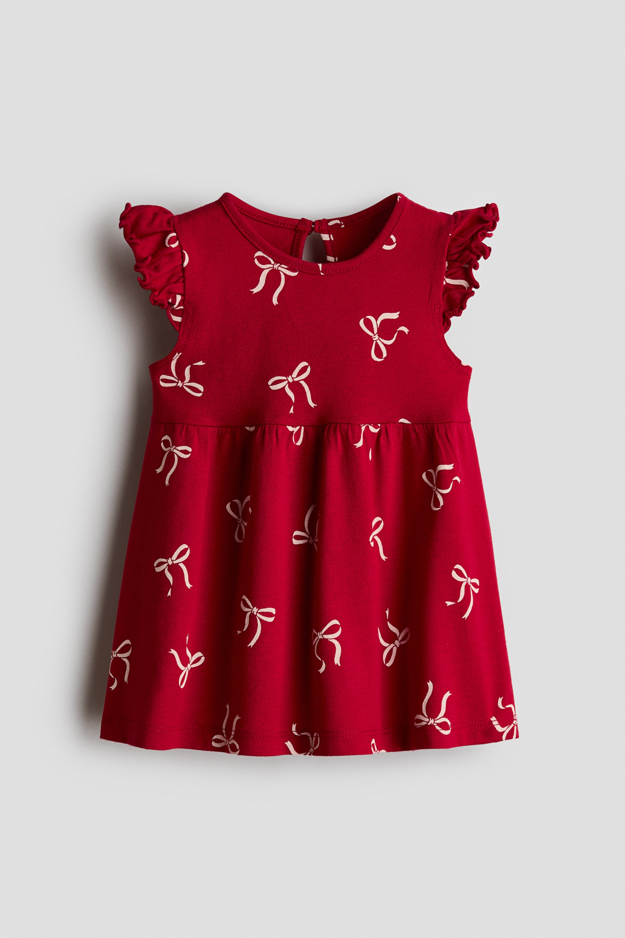 View larger image: A red cotton jersey dress is shown from the front, featuring an all-over print of small white bows. The dress is designed with a round neckline, ruffled flutter sleeves, gathers at the waist, and a flared skirt.