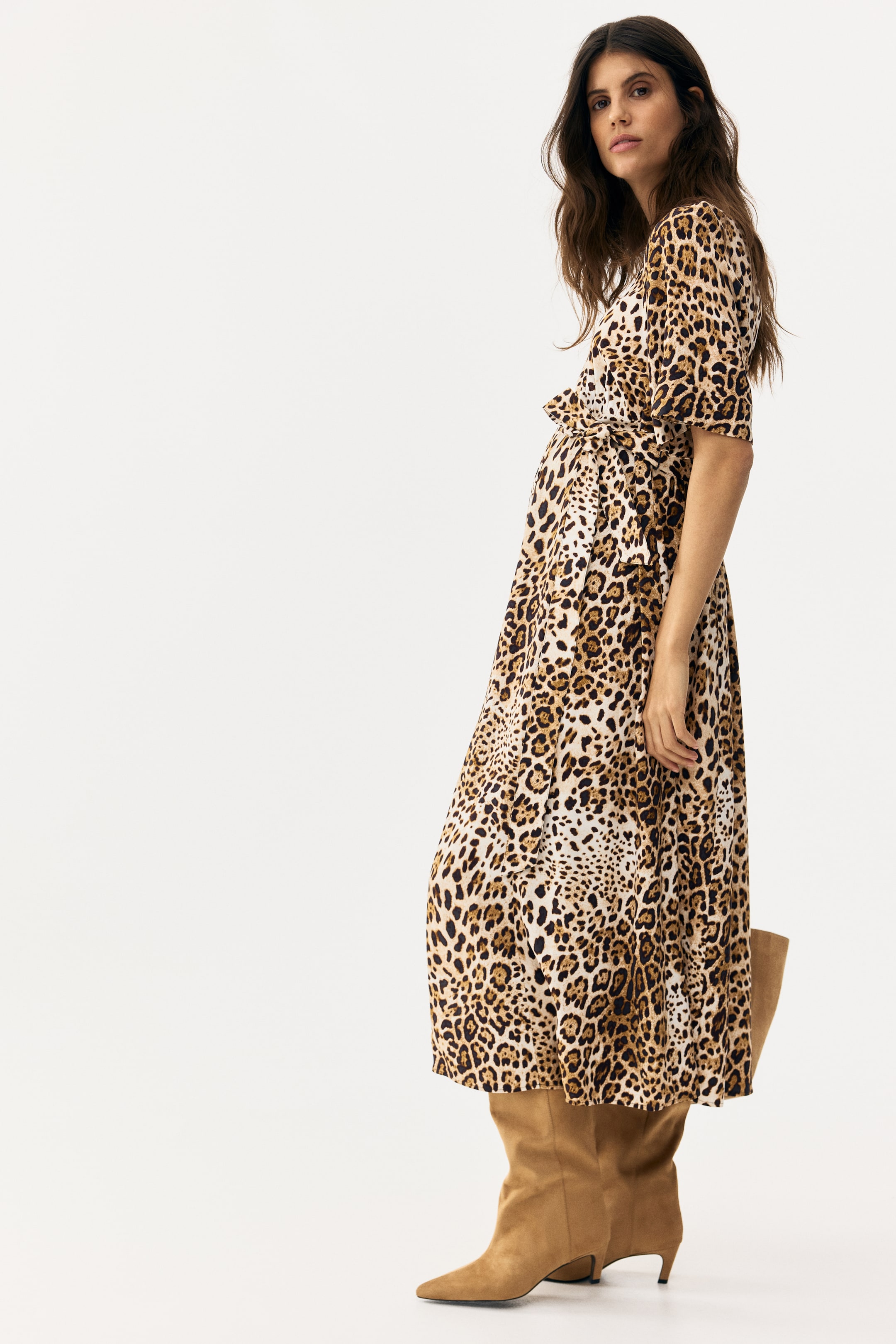 View larger image: The leopard print midi dress features a V-neckline, short gathered sleeves, and a self-tie waist, showcasing a flowing skirt and a wrap-style bodice from a slight side-front angle.