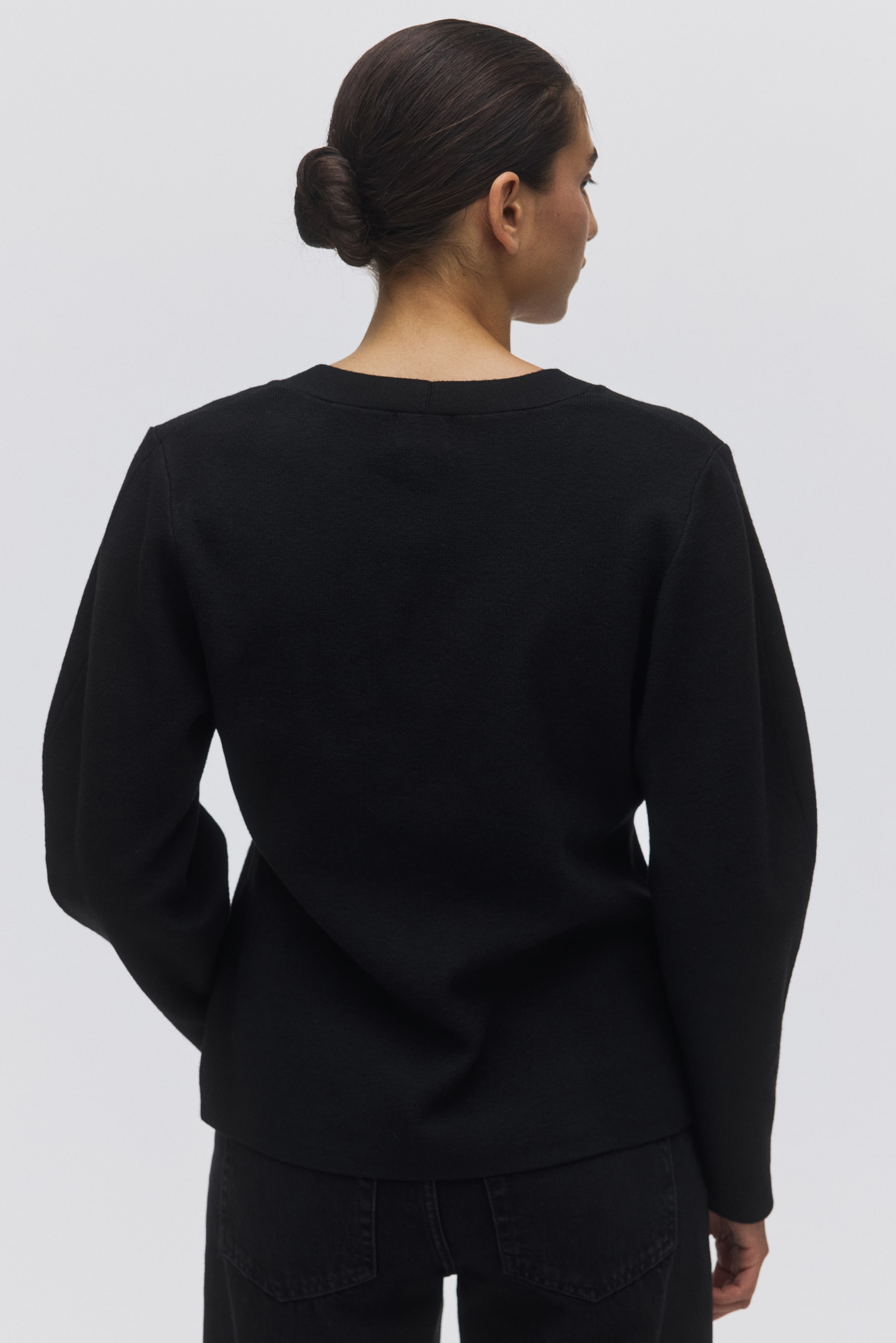 View larger image: A black textured knit top is being shown from the back. It features a crew neck and long, relaxed-fit sleeves with dropped shoulders, and falls to the hip over black jeans.