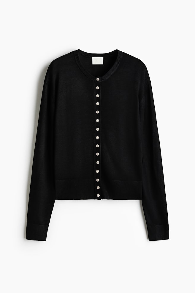 A black cardigan is displaying a round neck and a full button-front closure with small, light-colored buttons. It is featuring long sleeves with ribbed cuffs and a ribbed hem. - 1