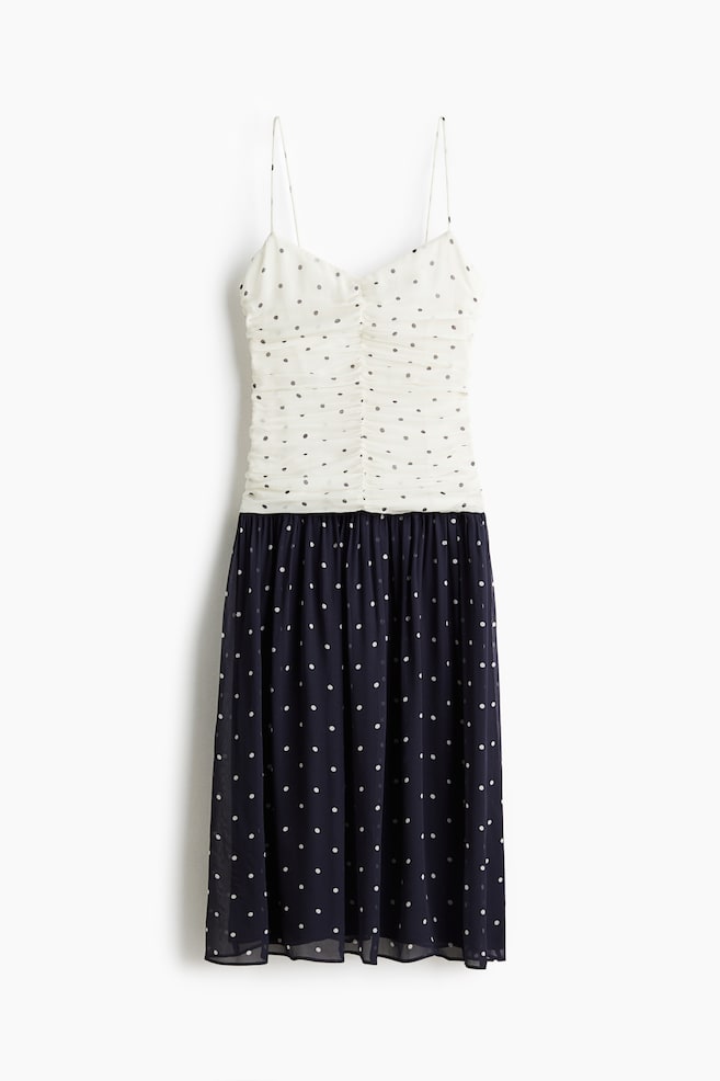 A dress is shown from the front, featuring an off-white, ruched camisole bodice with thin straps and small dark polka dots. Its lower section is a dark blue midi skirt, patterned with small white polka dots. - 1