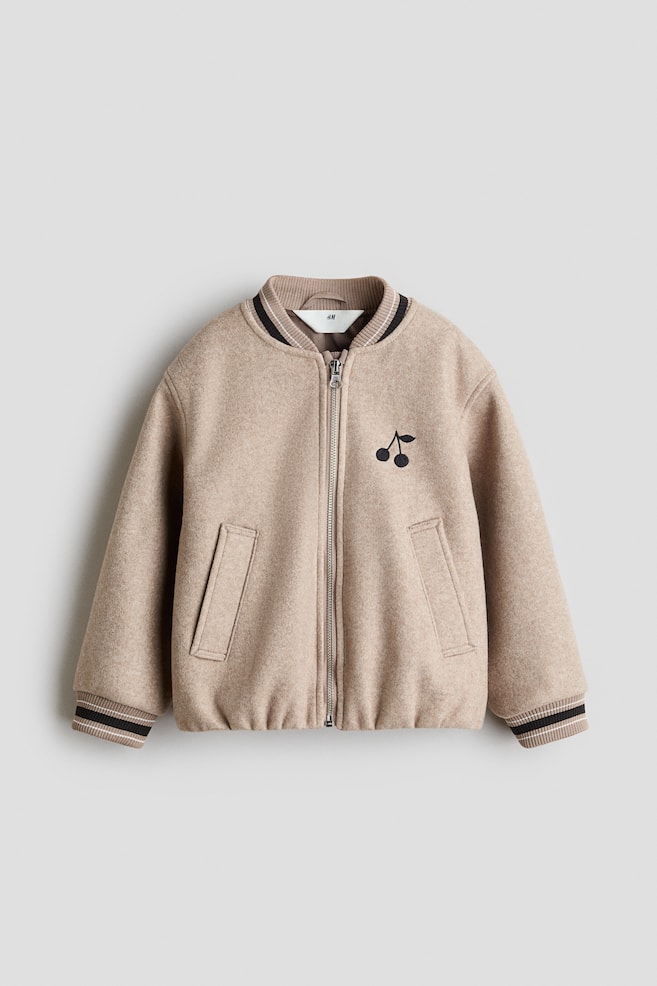 A beige felted bomber jacket is shown front-facing, featuring a full-zip closure and ribbed collar, cuffs, and hem, all detailed with black and white stripes. The jacket also showcases an embroidered black cherry motif on the left chest and two angled welt pockets at the front. - 1