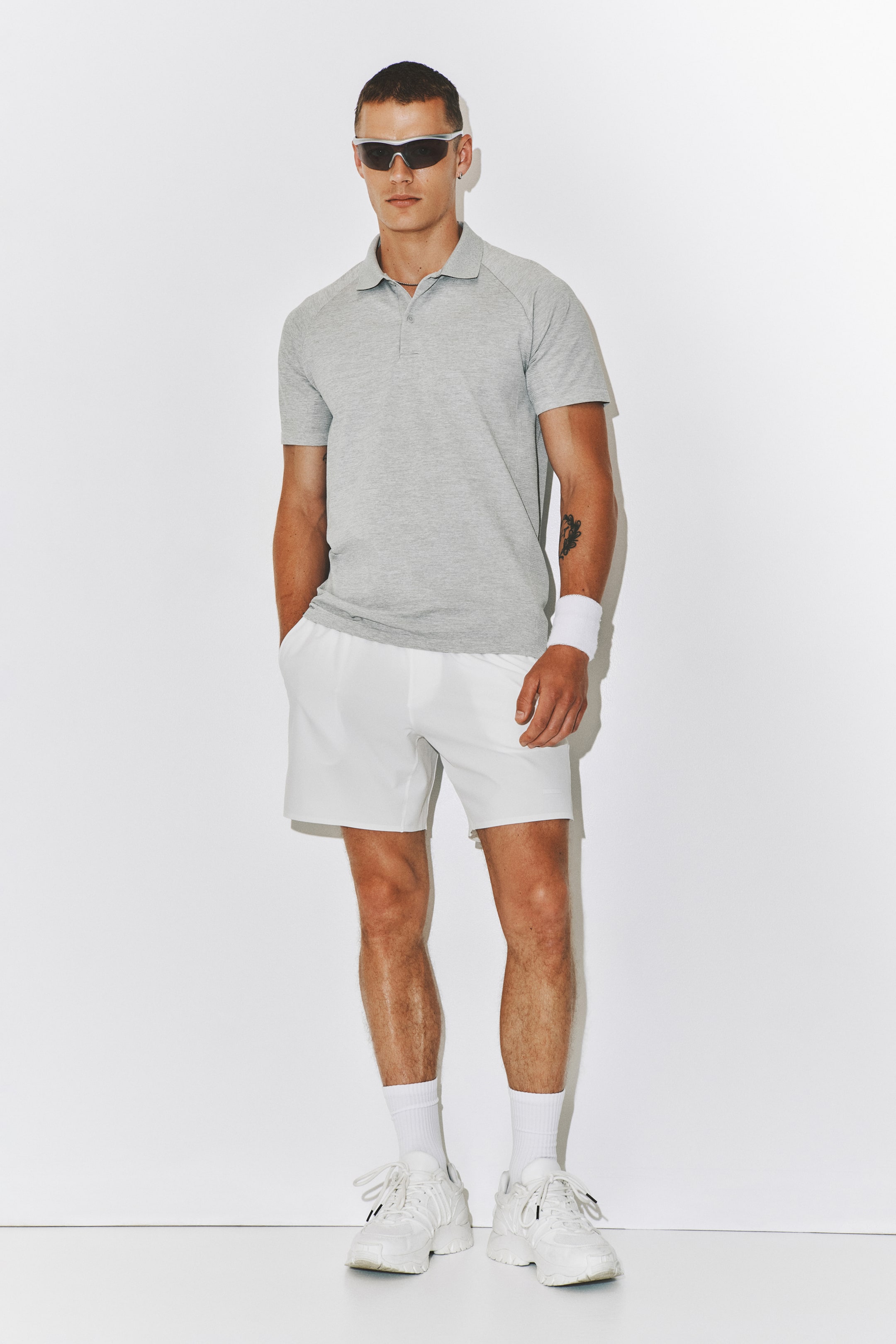 Größeres Bild anzeigen: Ein hellgraues Tennis-Poloshirt in regulärer Passform mit DryMove wird vom Modell getragen. Es verfügt über einen Kragen, eine Knopfleiste mit zwei Knöpfen und kurze Raglanärmel.