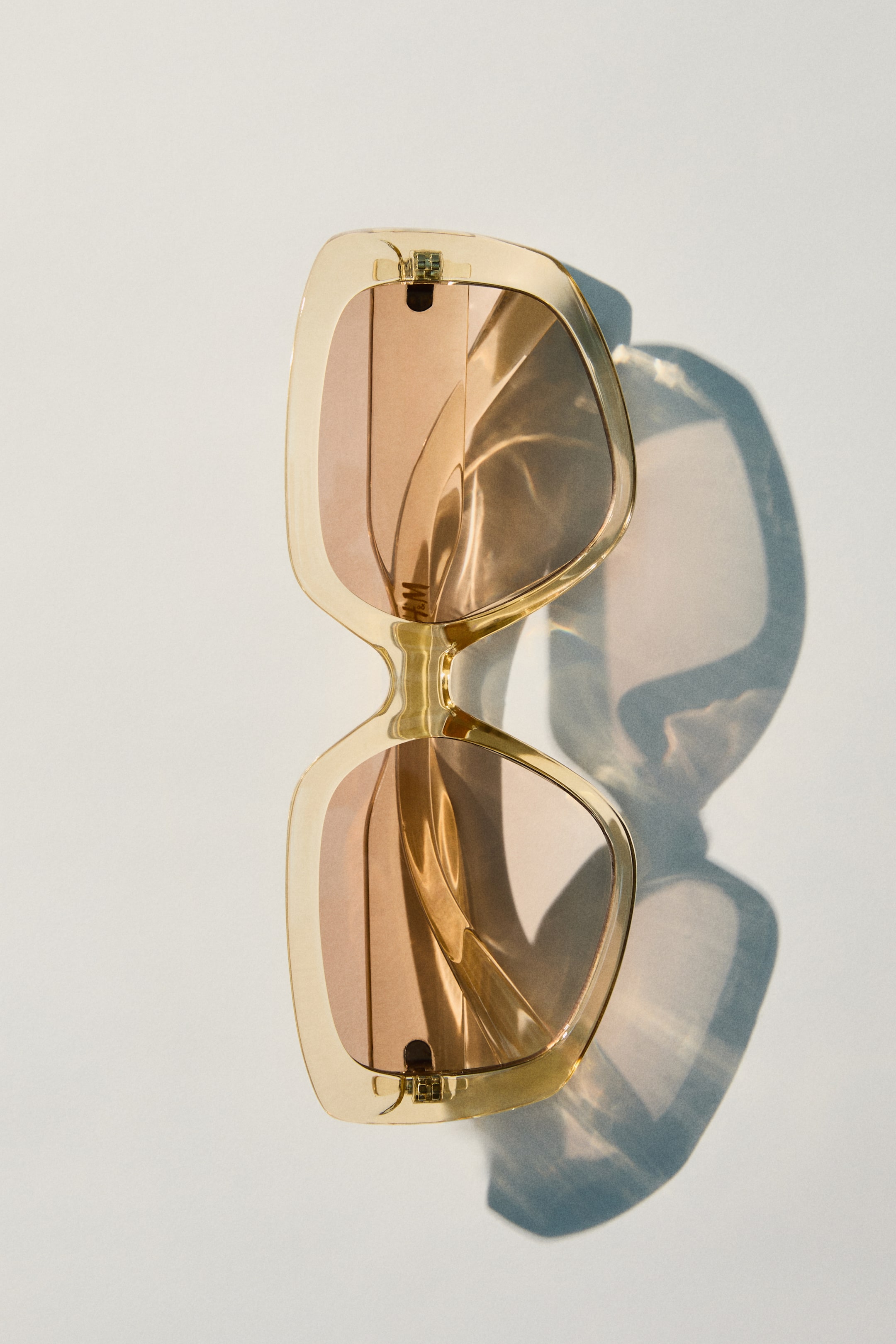 Voir une image plus grande: Lunettes de soleil carrées et larges avec des montures en plastique translucide beige clair et des verres teintés marron offrant une protection UV. Les lunettes de soleil sont présentées de face, avec les branches pliées vers l'intérieur, et un petit logo H&M est visible sur le verre droit.