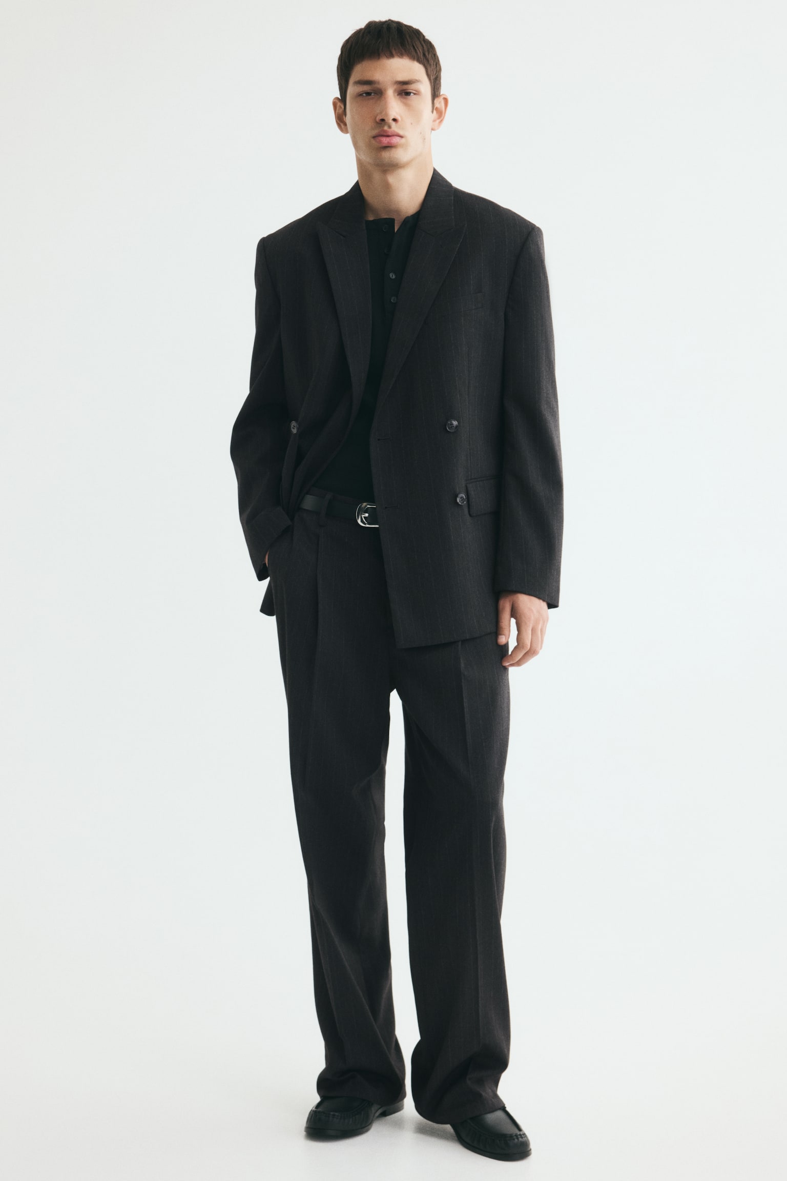 A dark grey pinstriped double-breasted blazer is facing front, featuring wide peak lapels. It is displaying four black buttons in two rows on the front, two flap pockets at the hip, and one welt pocket on the left chest, with three smaller black buttons on each cuff. - 1