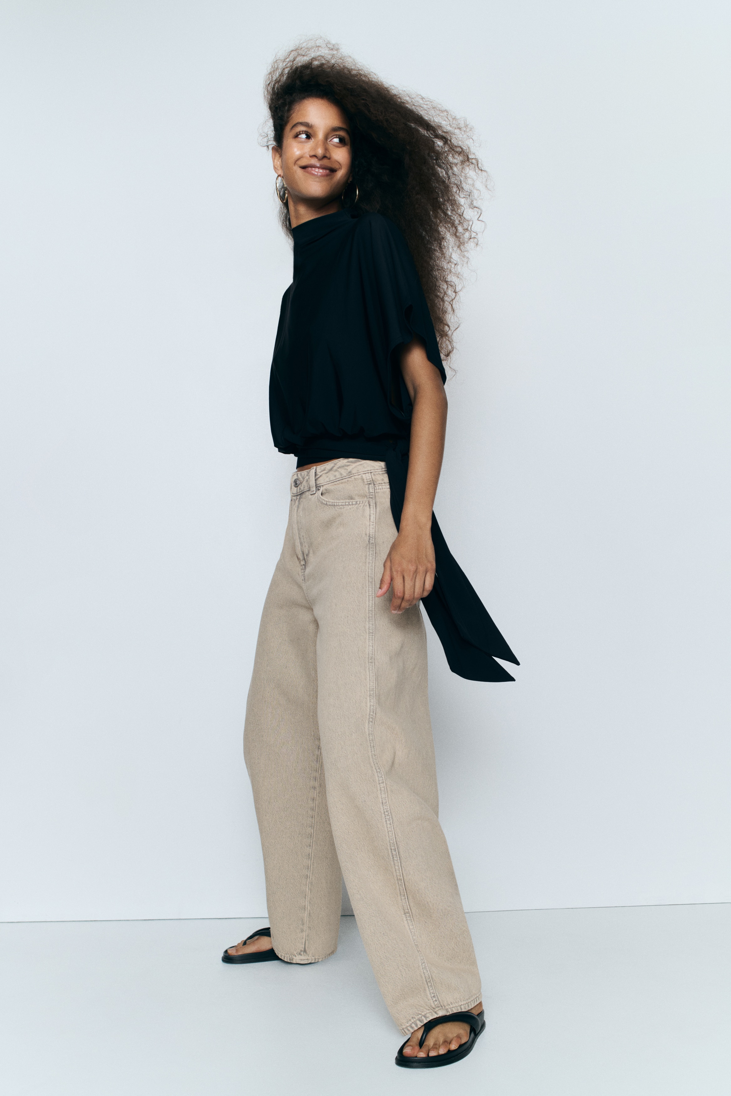 These light beige, acid-washed jeans showcase a high-waisted, wide-leg silhouette from the front. They feature front scoop pockets, belt loops, a button and zip fastening, and slightly frayed hems.