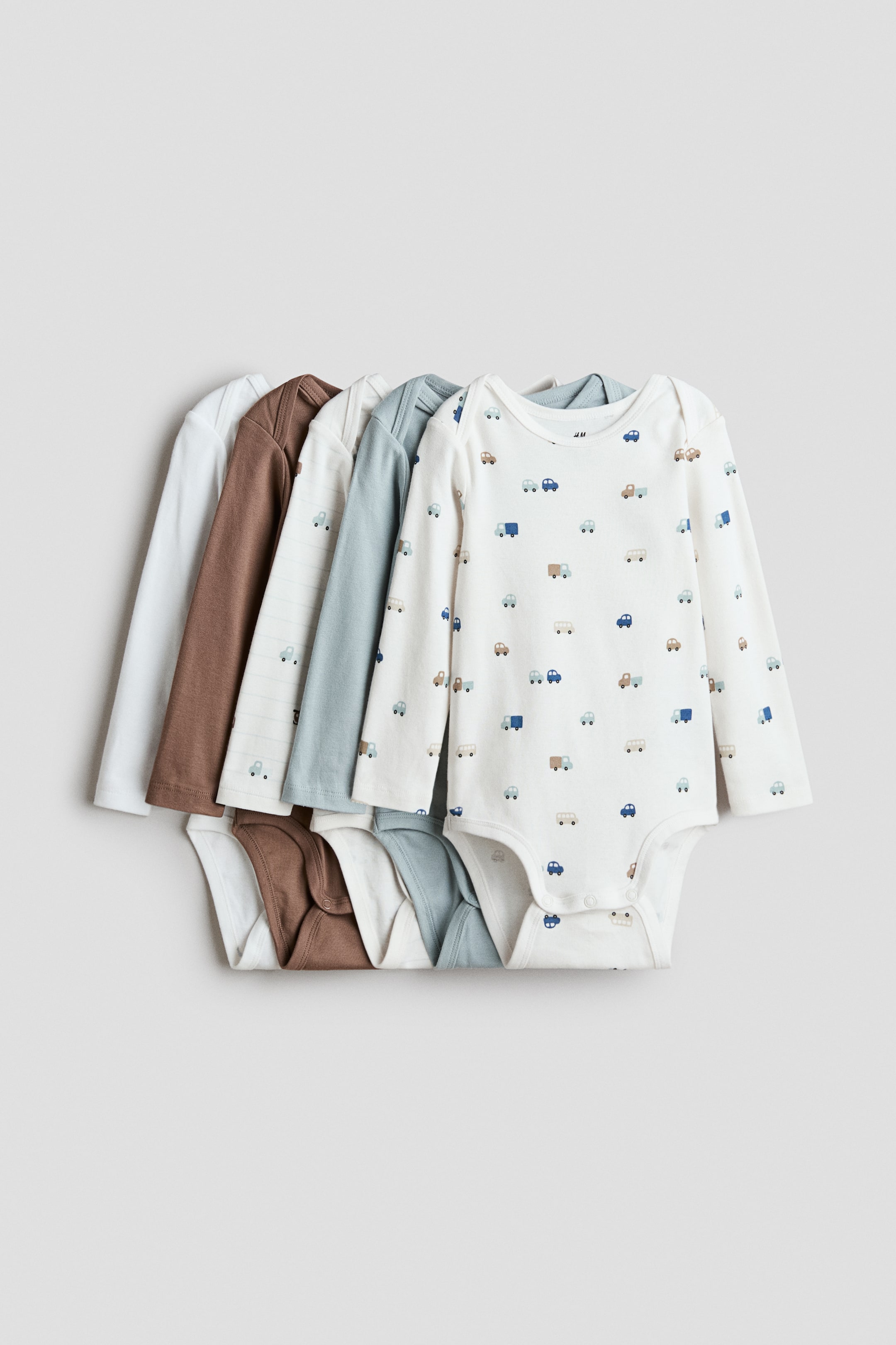 View larger image: Five long-sleeved bodysuits are stacked, with the front of the top bodysuit clearly visible. This top bodysuit features an envelope neck, press-studs at the bottom, and a cream colour with small car patterns, while the other bodysuits in the stack present varied designs and solid colours.
