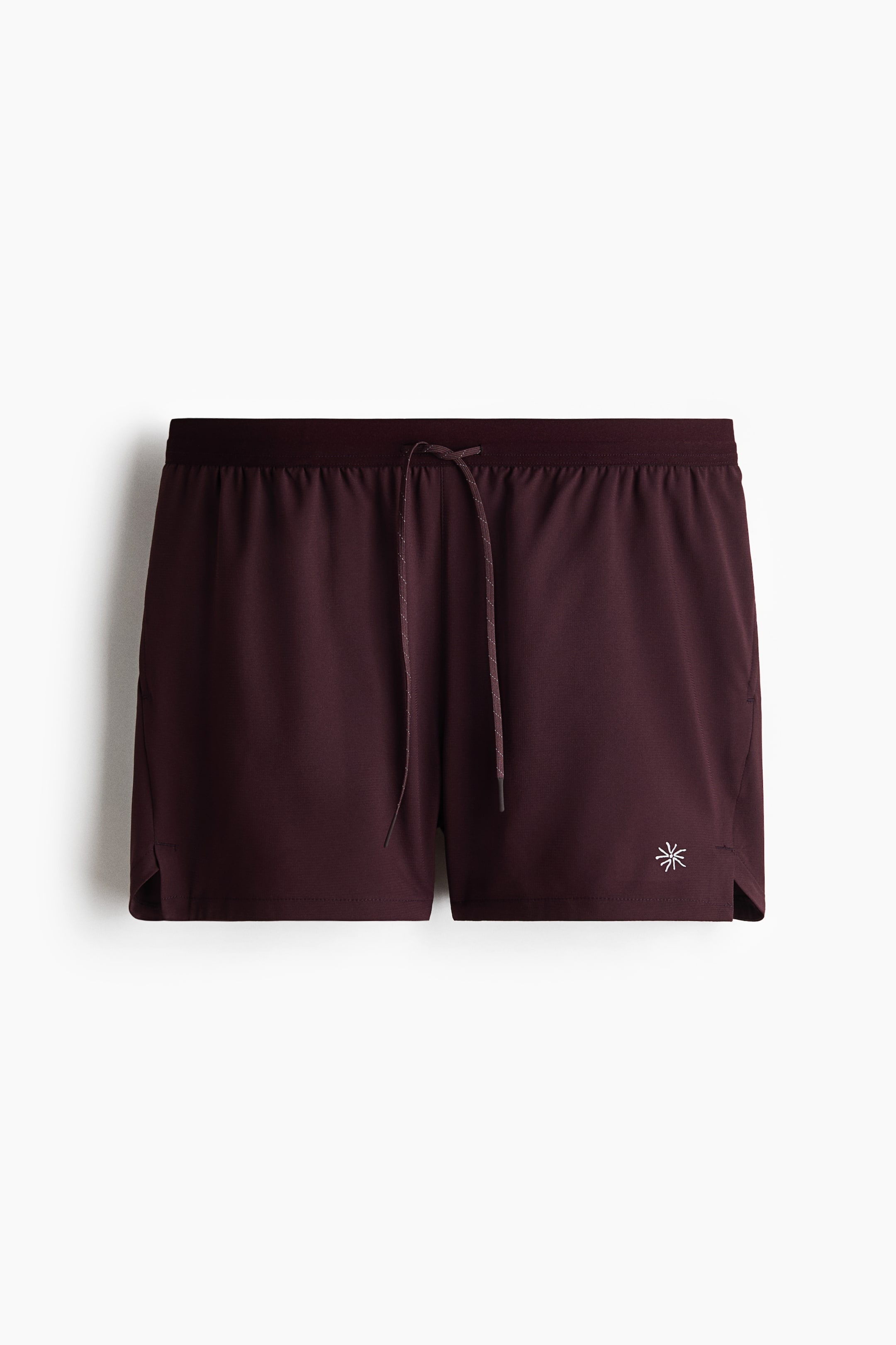 View larger image: Dark maroon athletic shorts are showcased facing forward, featuring an elastic waistband with a tied drawstring. A small white abstract logo is embroidered on the lower right leg, and small side slits are visible at the hem.