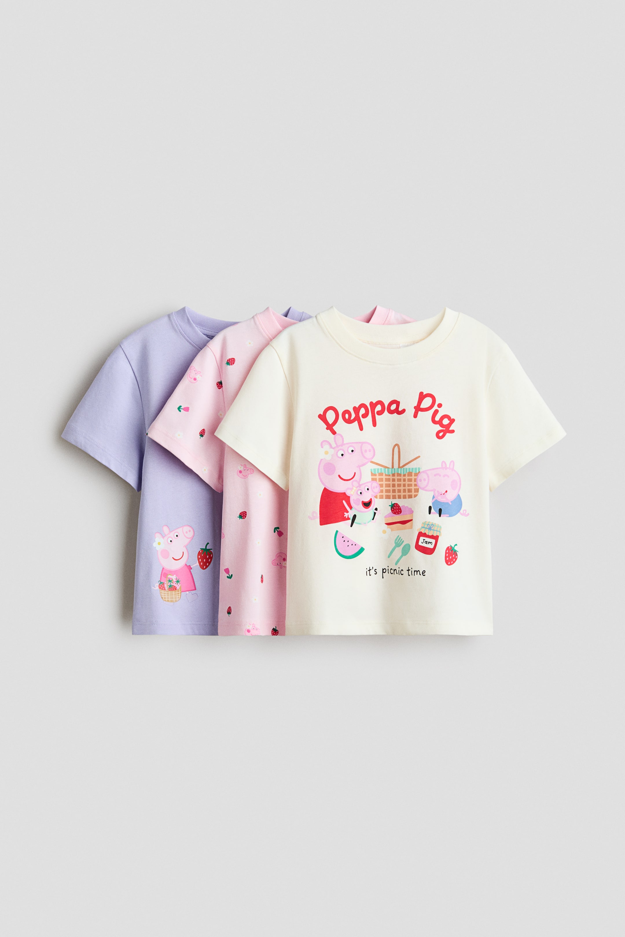 View larger image: Three short-sleeved jersey tops are shown from the front. The cream top features a 'Peppa Pig' picnic illustration, the pink top displays a repeating strawberry and Peppa Pig motif, and the purple top shows Peppa Pig holding a basket and a strawberry.