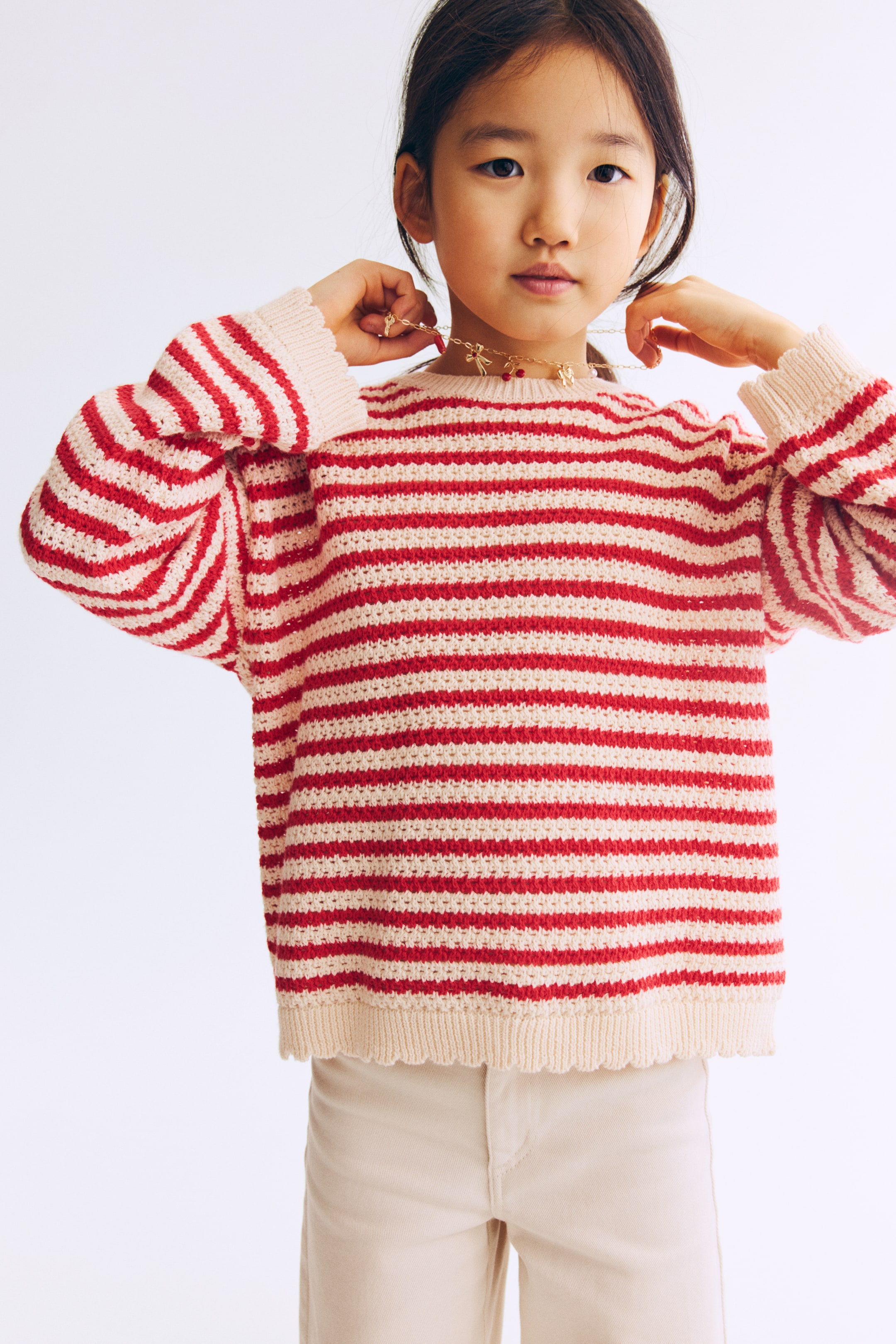 Xem ảnh lớn hơn: Chiếc áo len chụp chính diện được làm từ cotton dệt có kết cấu, với sọc ngang màu đỏ và kem. Thiết kế có cổ tròn viền bo, vai thụt và bo gợn sóng ở cổ tay và gấu áo.