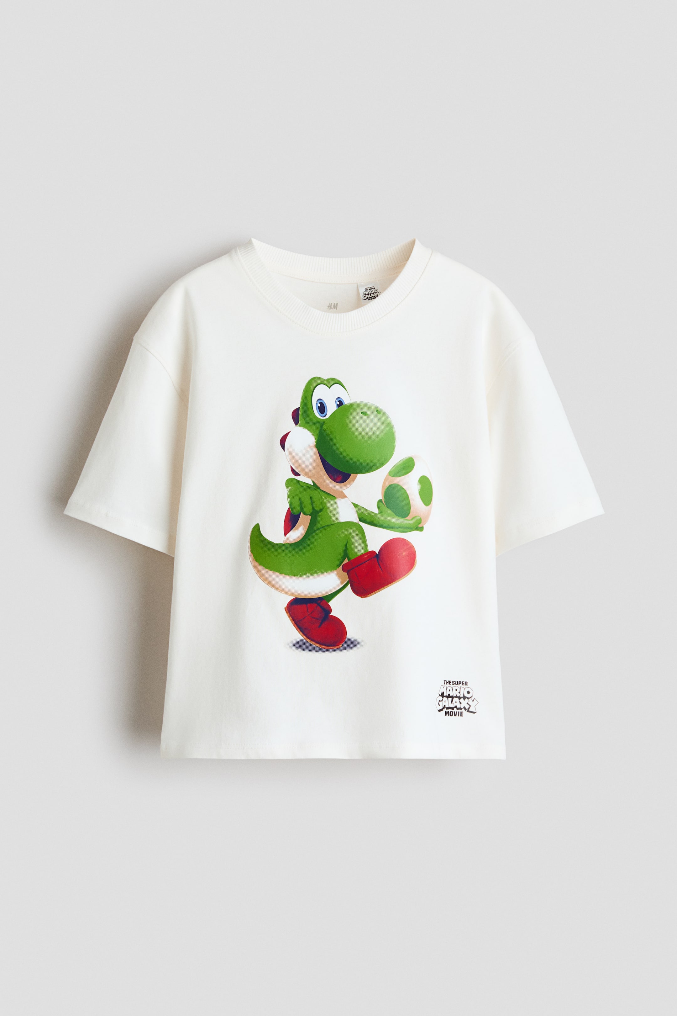 Προβολή μεγαλύτερης εικόνας: Ένα φαρδύ μπλουζάκι από μαλακό, τυπωμένο βαμβακερό ζέρσεϊ που εμφανίζει το μπροστινό του μέρος, με ένα μεγάλο γραφικό τύπωμα του πράσινου χαρακτήρα Yoshi που κρατά ένα πουά αυγό, με ριγέ φινίρισμα γύρω από το λαιμό και χαμηλωμένους ώμους.