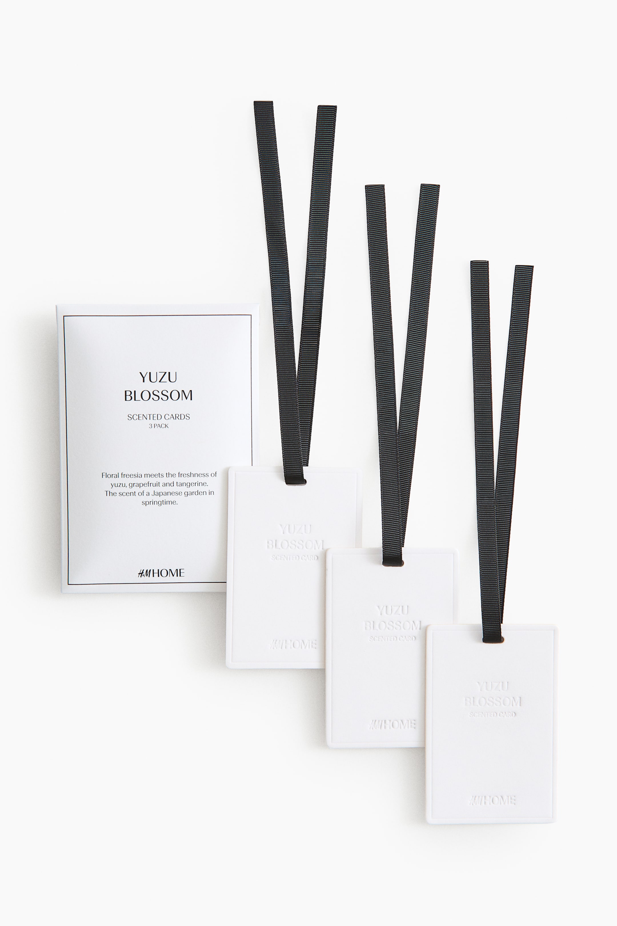 Agrandir l'image: Un ensemble de trois cartes parfumées rectangulaires blanches est présenté de face, chacune ornée d’un ruban gros-grain noir en haut et portant le texte en relief « YUZU BLOSSOM SCENTED CARD » et « H&M HOME ». Une boîte produit blanche est également visible, affichant « YUZU BLOSSOM SCENTED CARDS 3 PACK » ainsi que les détails du parfum.
