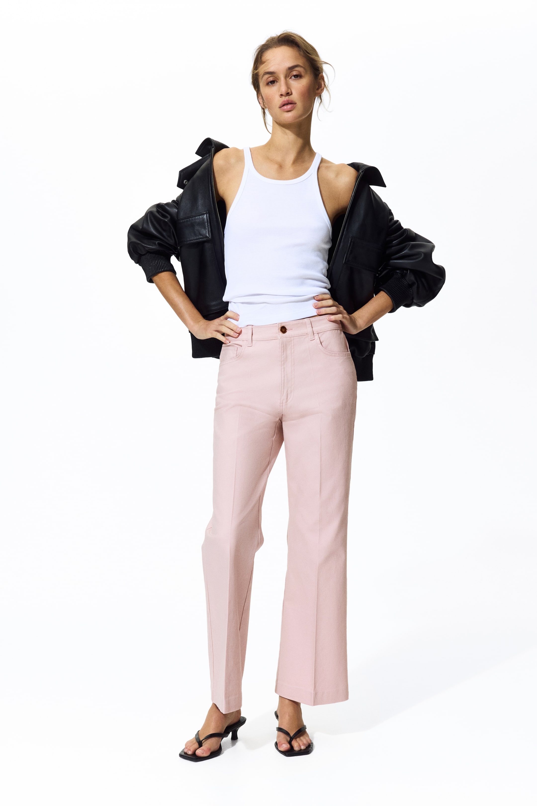 Ver imagem maior: Calças rosa apresentam um corte de cintura alta e perna reta com comprimento cropped. São desenhadas com um único botão castanho, presilhas para cinto, bolsos frontais curvados e costuras verticais proeminentes ao longo da frente de cada perna.