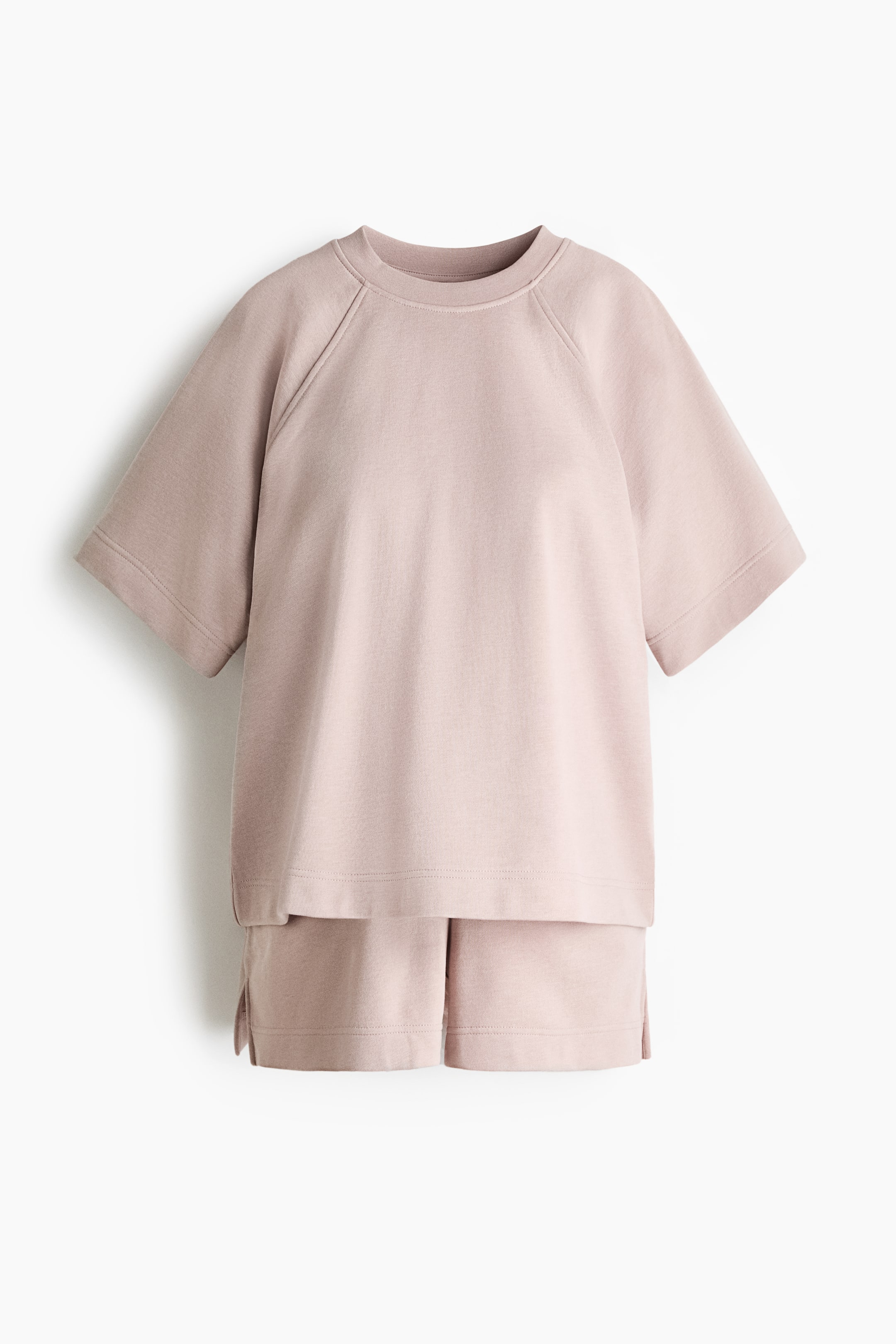 Größeres Bild ansehen: Ein T-Shirt- und Shorts-Set aus leichtem Sweatshirtstoff wird von vorne präsentiert. Das T-Shirt verfügt über einen Rundhalsausschnitt, Raglanärmel und einen gerade geschnittenen Saum mit einem Schlitz an jeder Seite, während die Shorts eine niedrige Taille mit Gummizug und kleine Schlitze an den Säumen aufweisen.