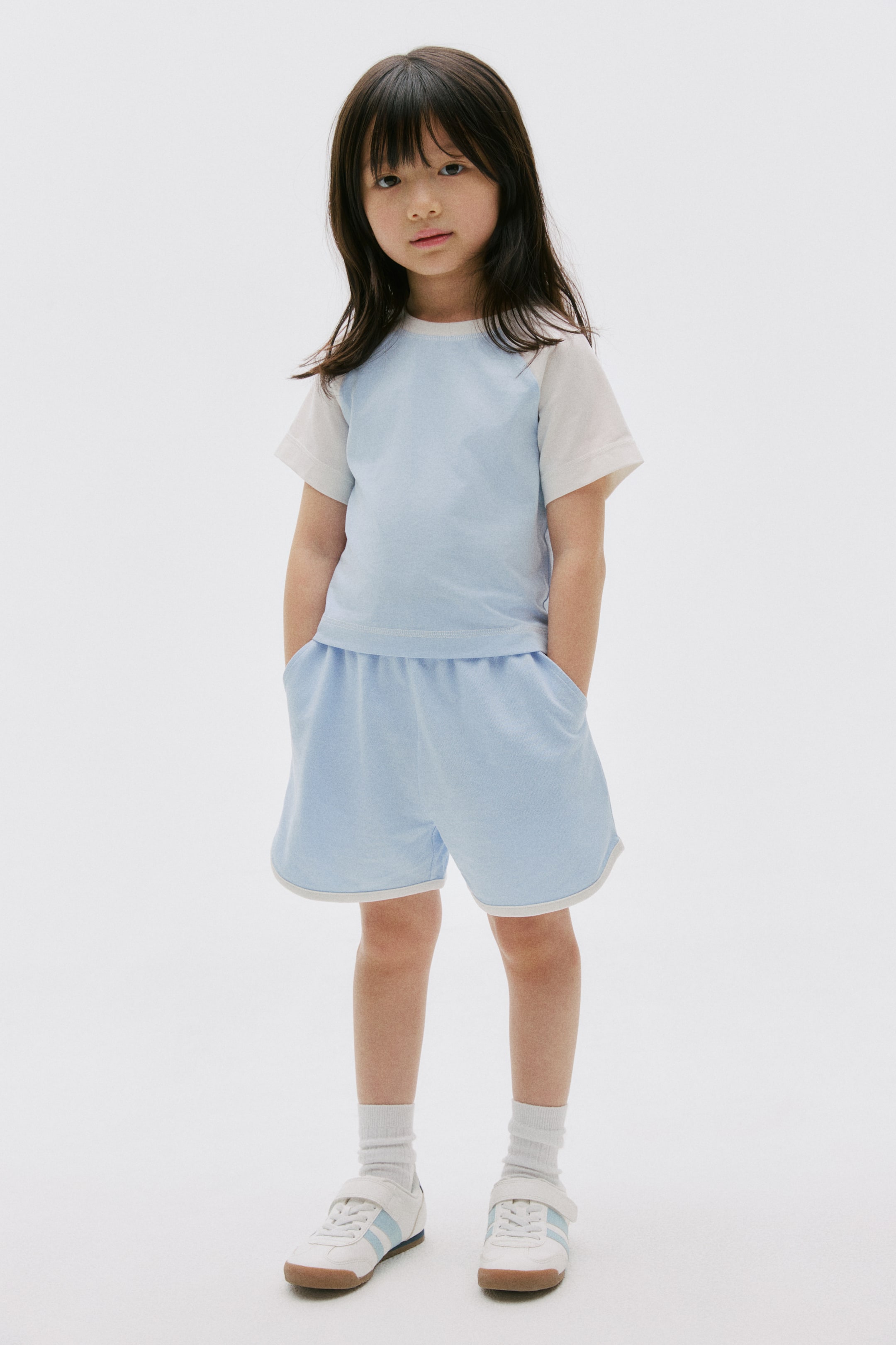 View larger image: A two-piece set is featuring a light blue and white raglan t-shirt with a light blue crew neck and short sleeves. It is paired with matching light blue shorts, which are designed with an elasticated waistband, side pockets, and white piping along the hem.