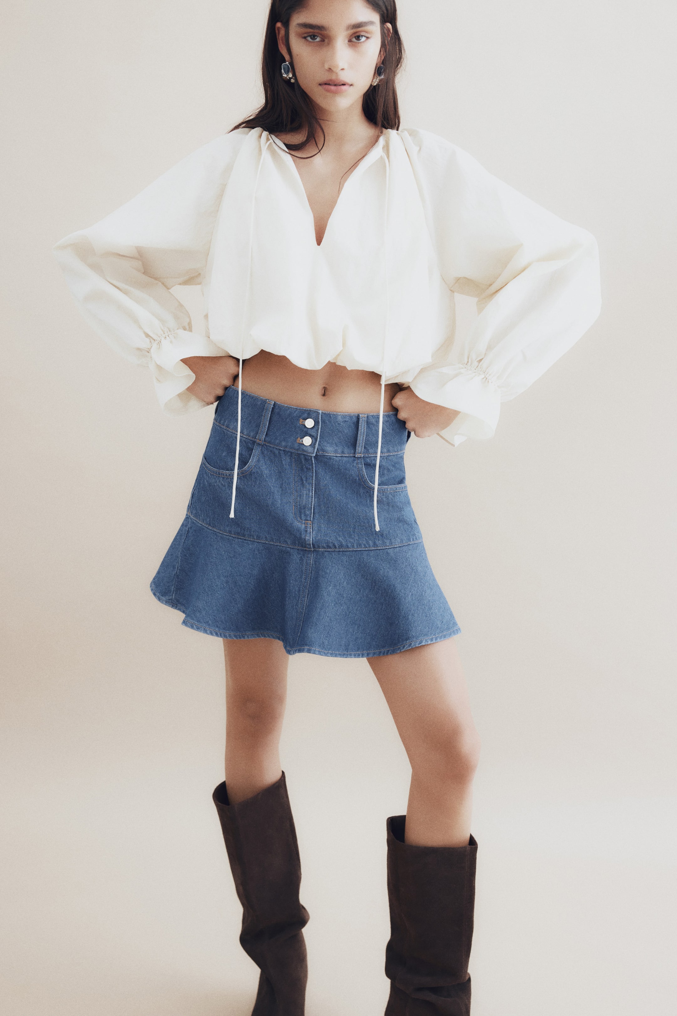 View larger image: A blue denim mini skirt is showcased from the front, boasting a high waist with a double button closure and belt loops. It is crafted with two front pockets and an A-line silhouette, flaring out below a horizontal seam.