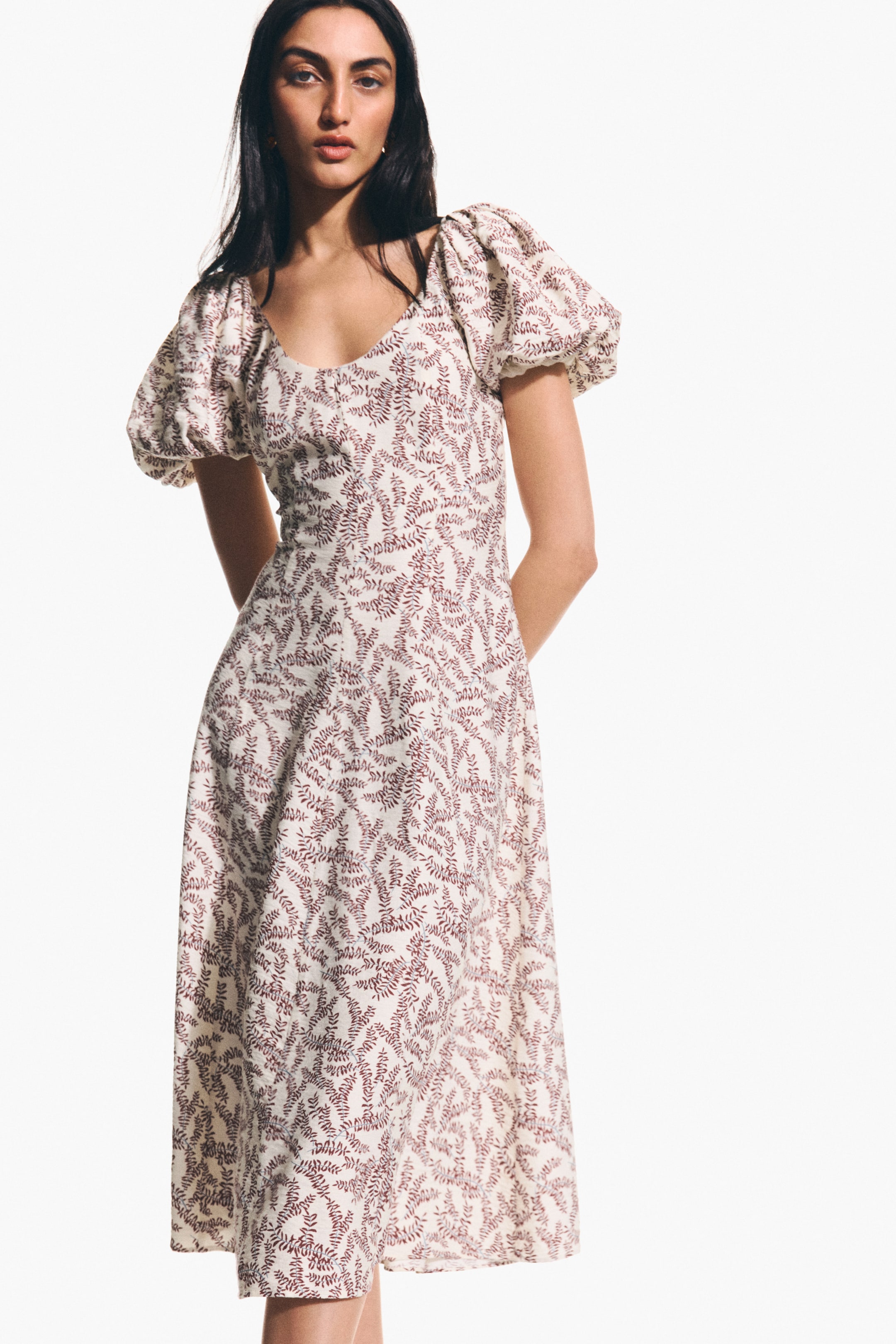 View larger image: A white midi dress with a reddish-brown leaf pattern is shown from a front angle. It features a sweetheart neckline, short puff sleeves, and a fitted bodice that flows into an A-line skirt.
