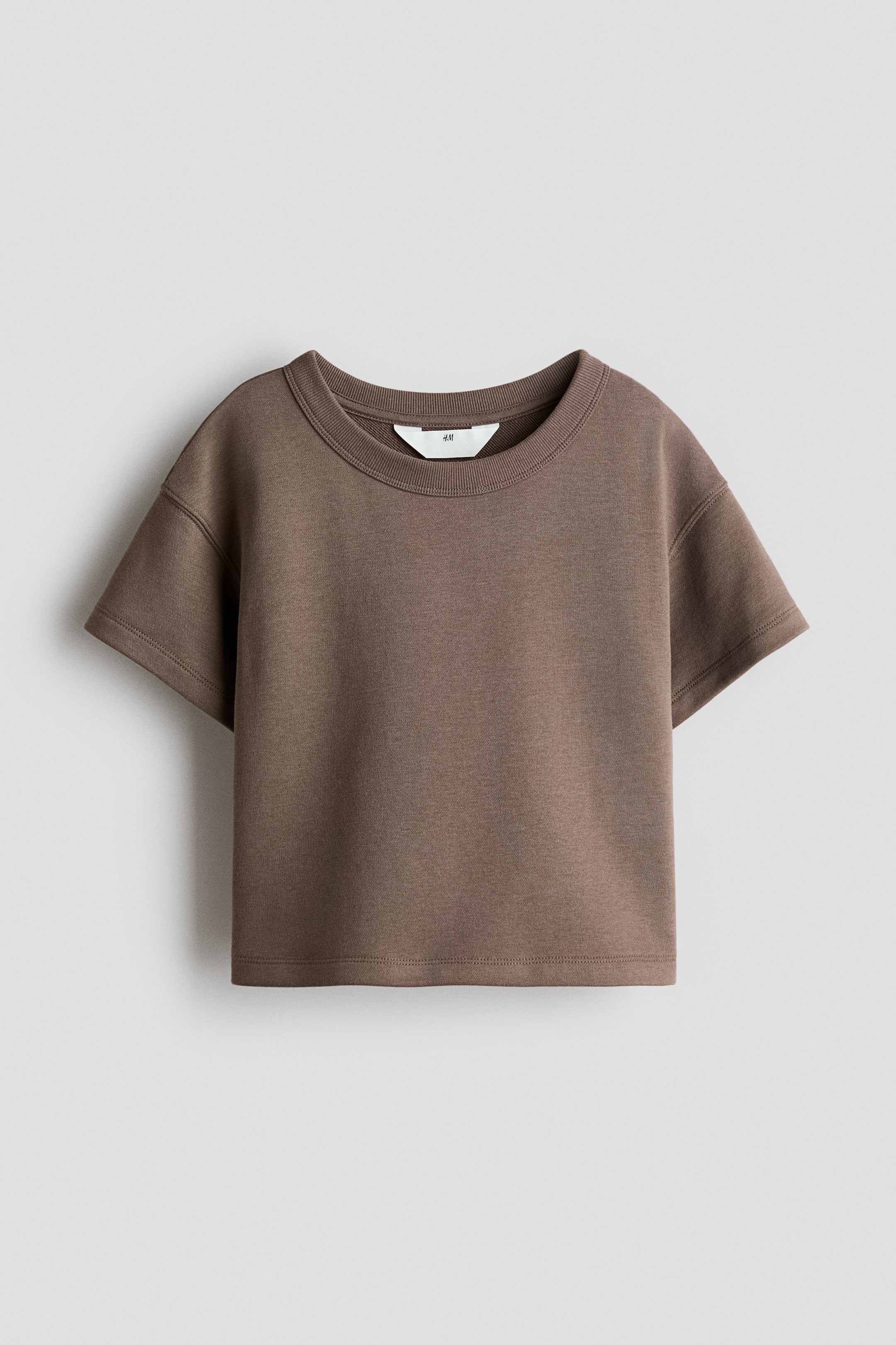 Agrandir l'image: Un haut ample en tissu de sweat léger marron se présente à l'avant, avec un col rond bordé de côtes, des épaules tombantes et des manches courtes.