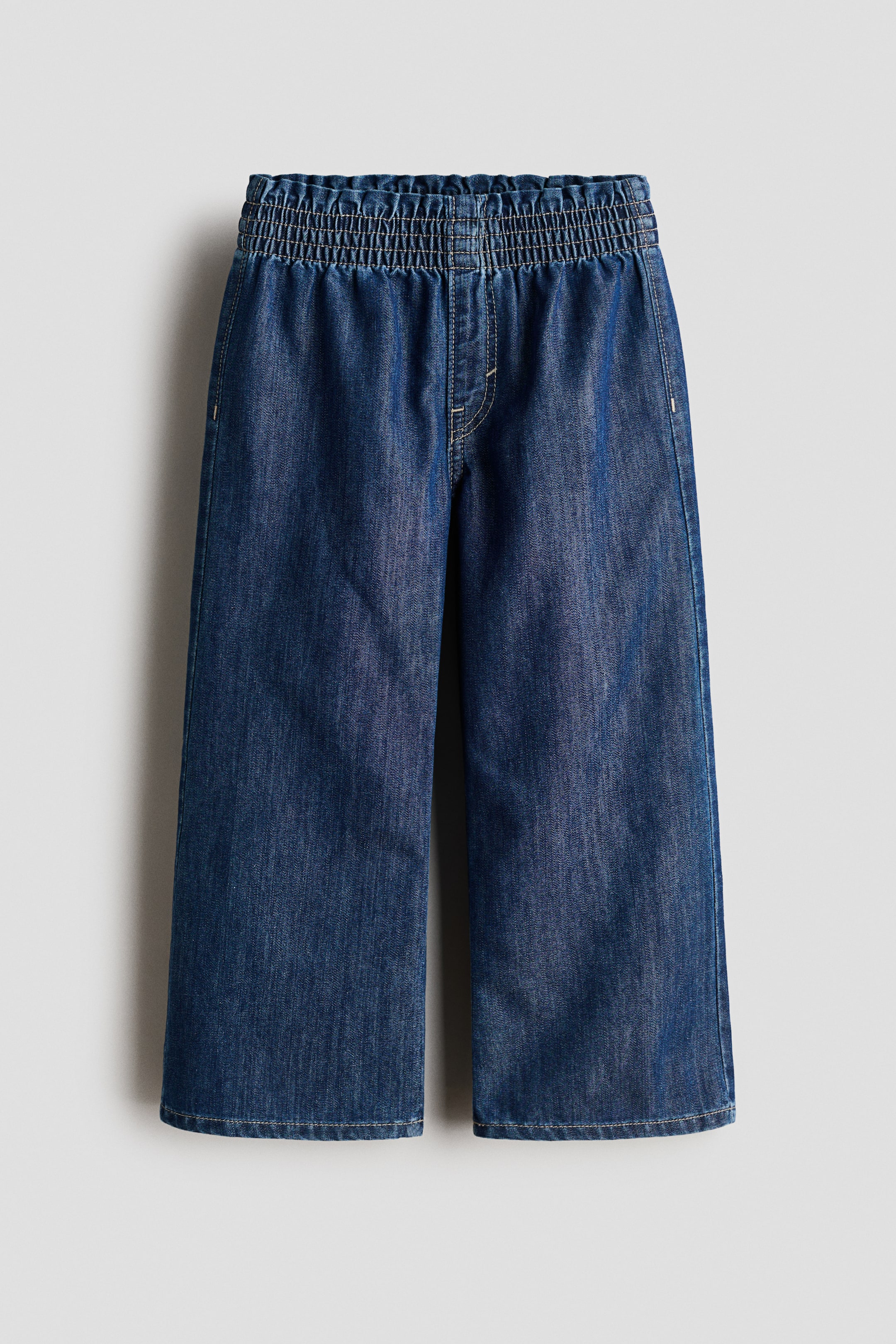 查看大圖: 深藍色牛仔褲,特色包括彈性褶皺腰帶、寬鬆褲腿和淺色縫線細節,從正面展示。