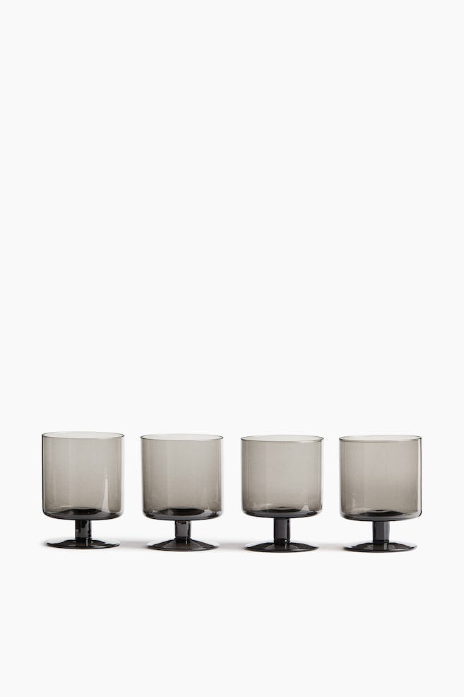 Quatre gobelets à pied en verre soufflé à la bouche, teintés dâun gris fumé, sont alignés horizontalement vus de face, mettant en valeur leur design cylindrique à parois droites, leurs courtes tiges épaisses et leurs bases circulaires plates. - 1