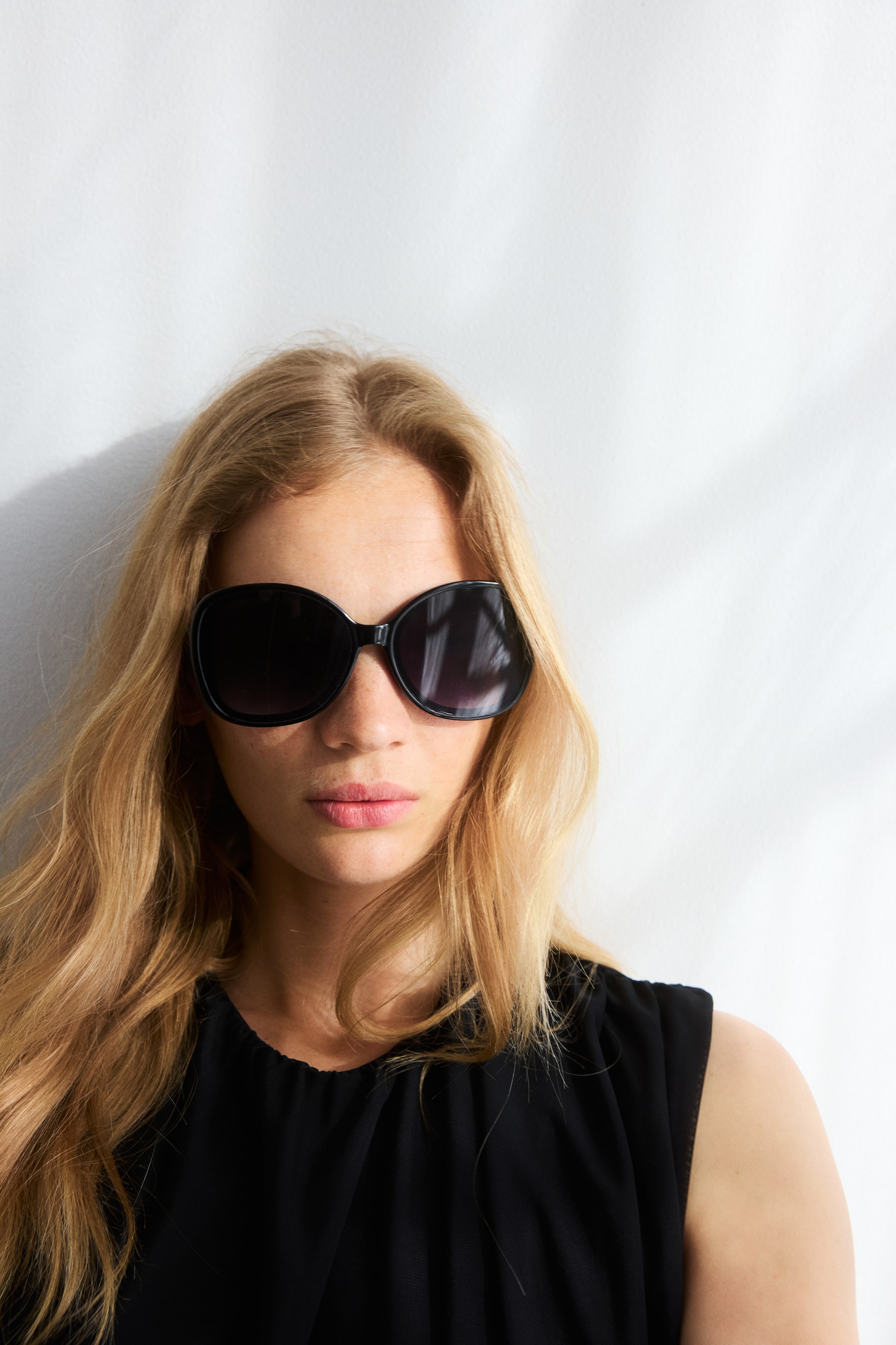View larger image: Square sunglasses with black plastic frames and sidepieces, featuring tinted, UV-protective plastic lenses, are being worn by the model.