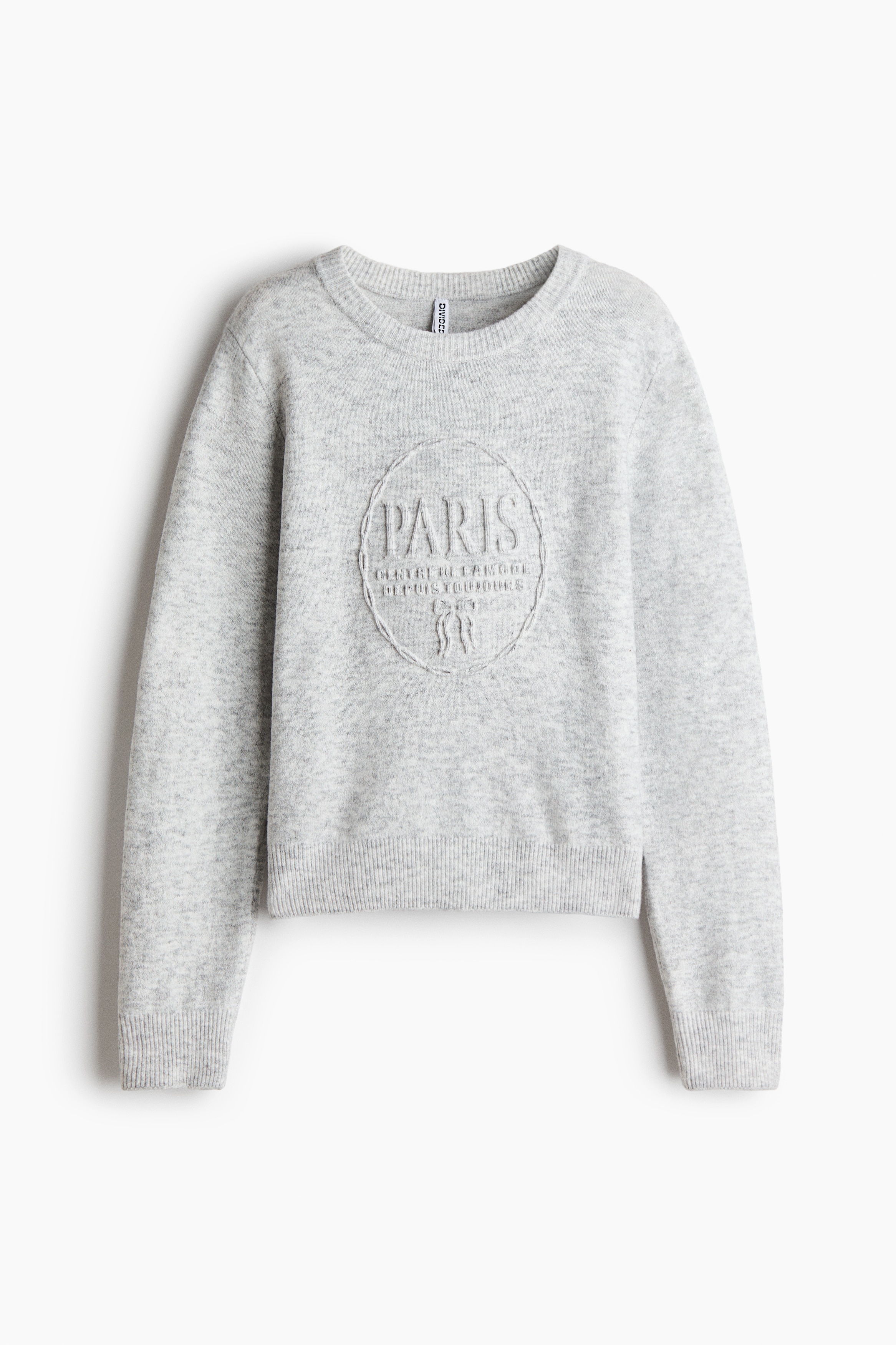 A light grey fine-knit sweater featuring an embossed circular design with "PARIS" text on the chest is being worn by the model. The sweater features a round ribbed neckline and ribbed cuffs and hem, and is styled with light blue denim jeans.