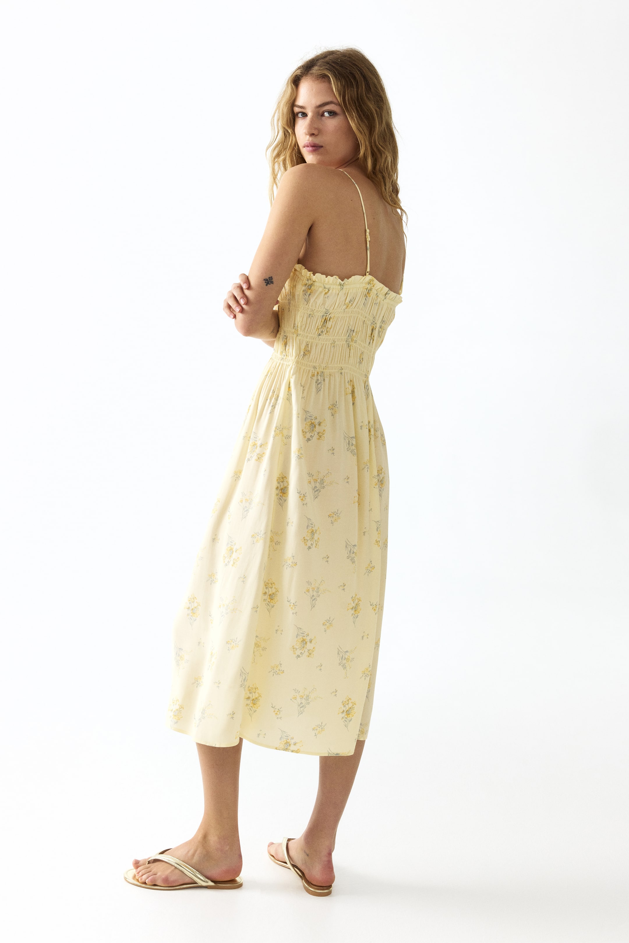 View larger image: The model is wearing a calf-length dress with a light floral pattern. This dress features a square neckline, adjustable spaghetti shoulder straps, a smocked bodice, and a flared skirt.