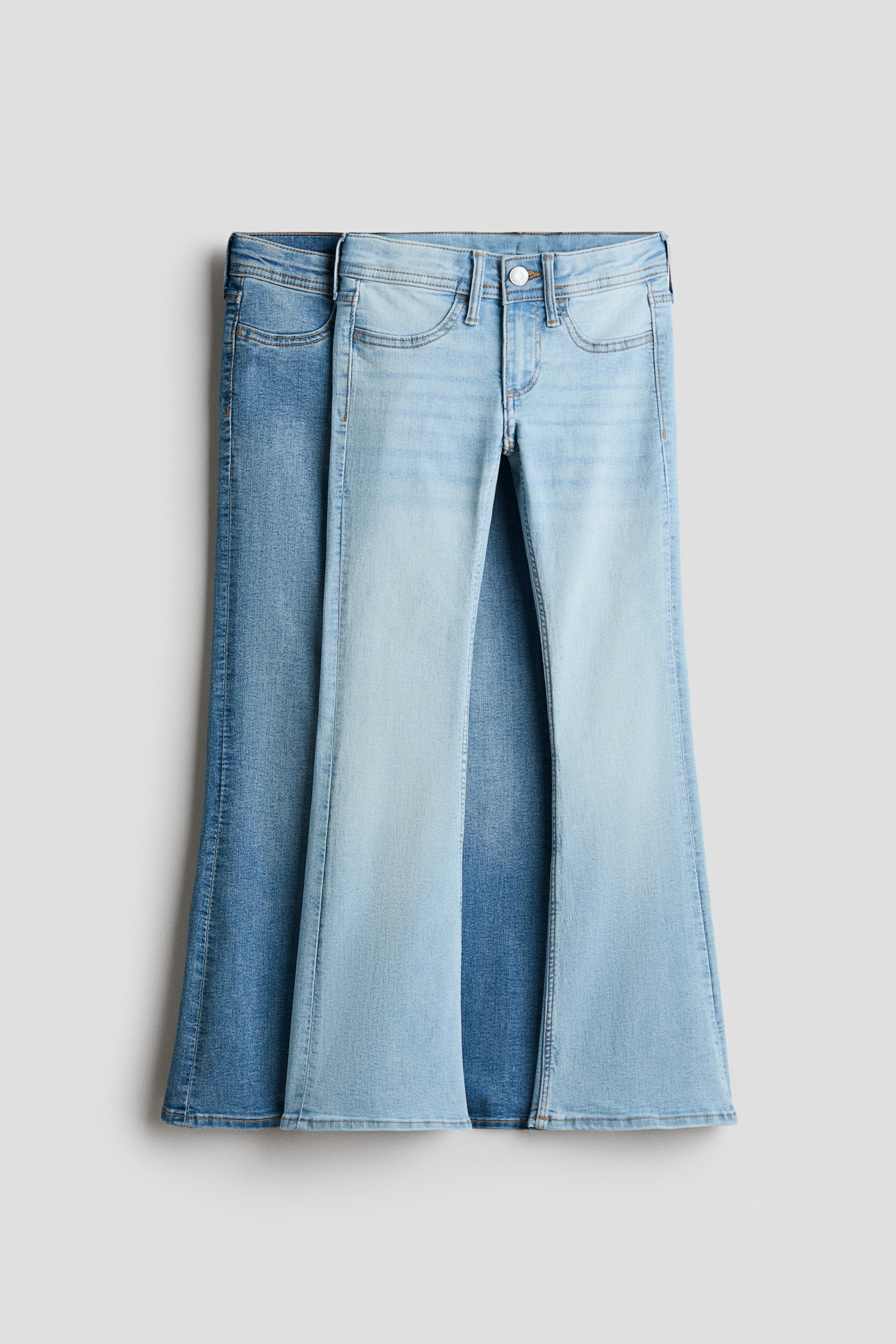 Größeres Bild anzeigen: Jeans präsentieren sich frontseitig, mit einem zweifarbigen gewaschenen Denim, das vorne hellblaue Panels und an den Seiten dunkleres Blau sichtbar zeigt. Sie sind mit einer engen Passform an Hüfte und Oberschenkel entworfen, die sich zu den Beinen hin deutlich ausstellt, mit einer niedrigen Taille, einem Reißverschluss mit Knopfverschluss und zwei gesteppten Fake-Taschen vorne.