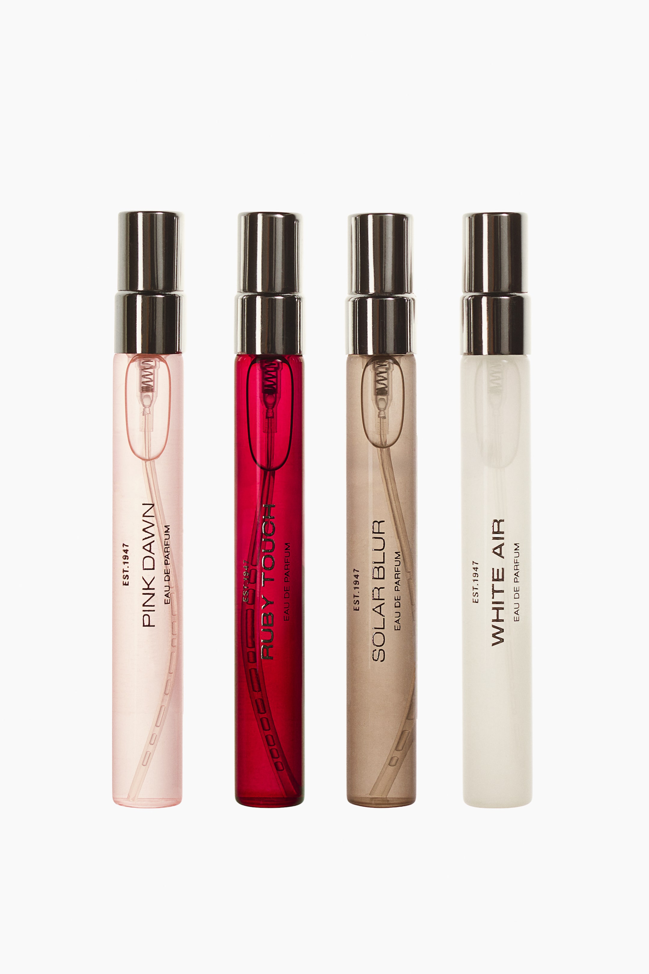 View larger image: The Discovery Set Eau De Parfum features four slim, cylindrical glass vials arranged side by side, facing forward. Each vial contains a differently coloured liquid—pink, red, light brown, and clear—and displays vertical black text showing its fragrance name beneath a metallic silver spray nozzle.