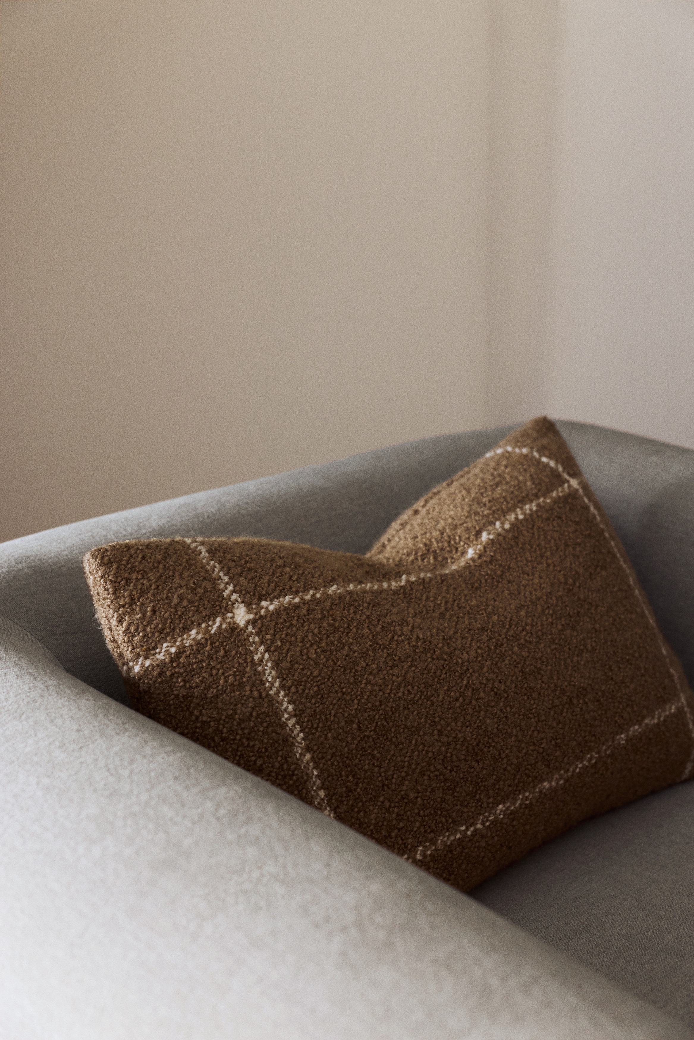 A rectangular pillow features a textured brown boucle fabric on its front, showcasing a light-coloured windowpane plaid pattern.