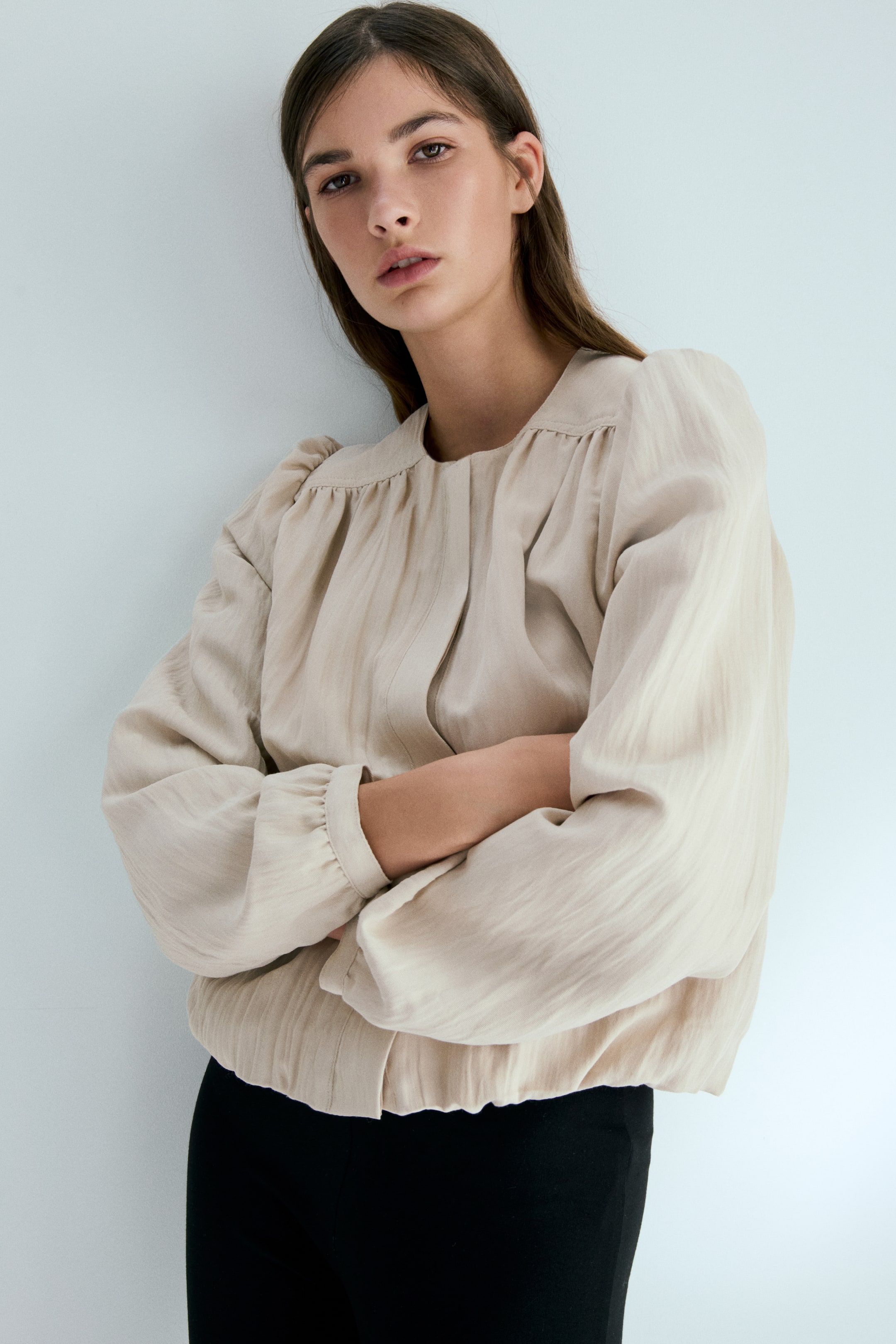 View larger image: The model is seen sporting an oversized light beige jacket crafted from textured fabric. It showcases a round neckline, a gathered front yoke, long puff sleeves, and an elasticated gathered hem. The model is posed with arms crossed, pairing the jacket with black bottoms.