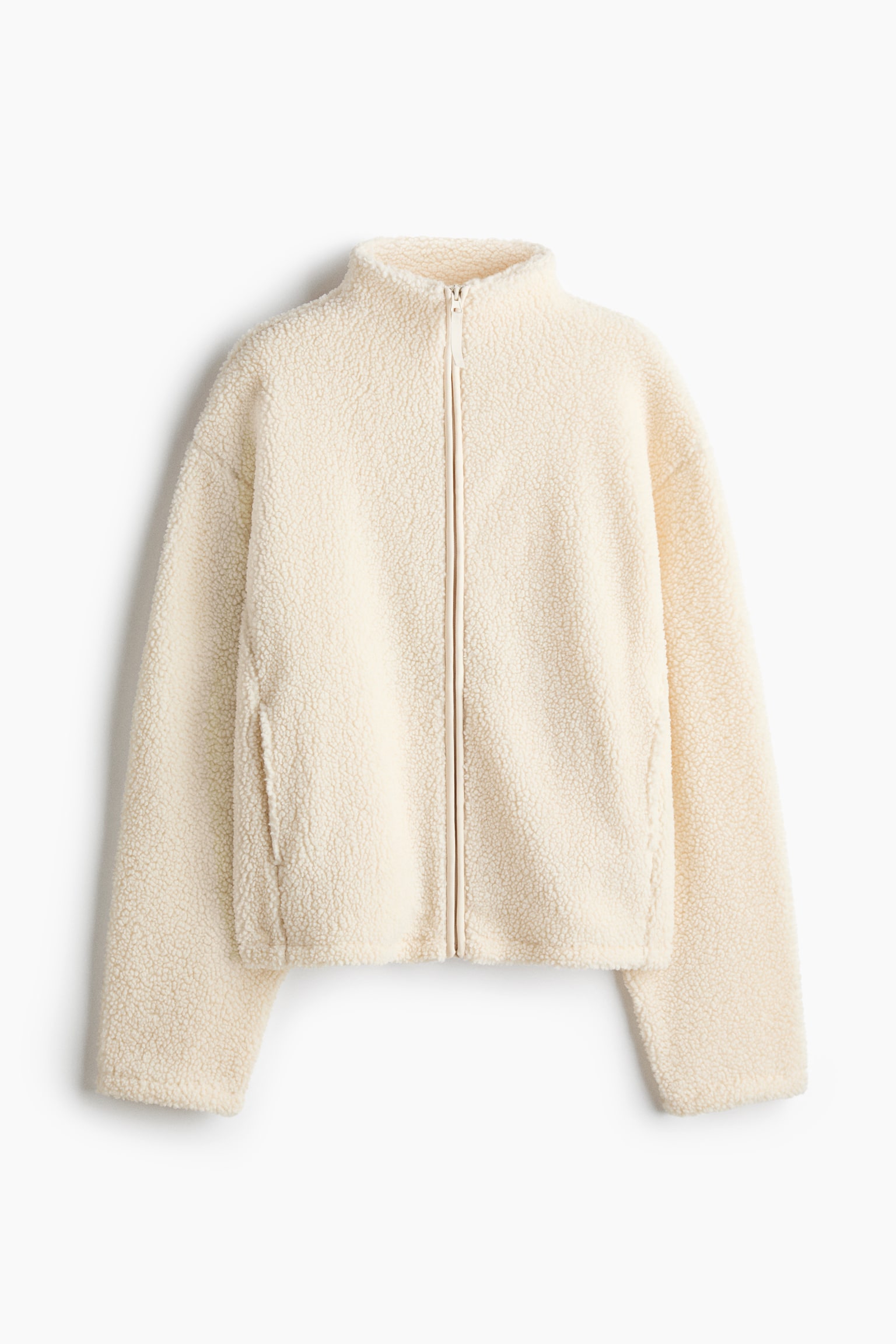 Denne cremefarvede teddy fleecejakke vender mod fronten og har en hÃ¸j opretstÃ¥ende krave, en gennemgÃ¥ende lynlÃ¥s foran samt lange Ã¦rmer med sÃ¦nkede skuldre. Jakken fremhÃ¦ver et struktureret, krÃ¸llet fleece-materiale og har diskrete paspolerede sidelommer. - 1