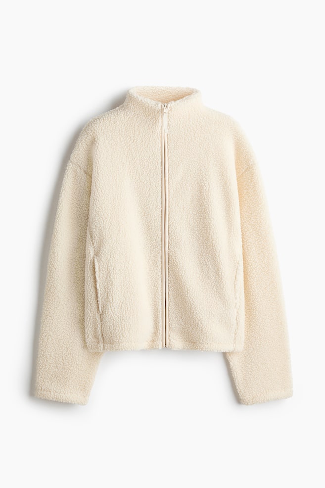 This cream-colored teddy fleece jacket is facing the front, featuring a high stand-up collar, a full-length front zipper, and long sleeves with dropped shoulders. The jacket is displaying a textured, curly fleece fabric and includes subtle side welt pockets. - 1