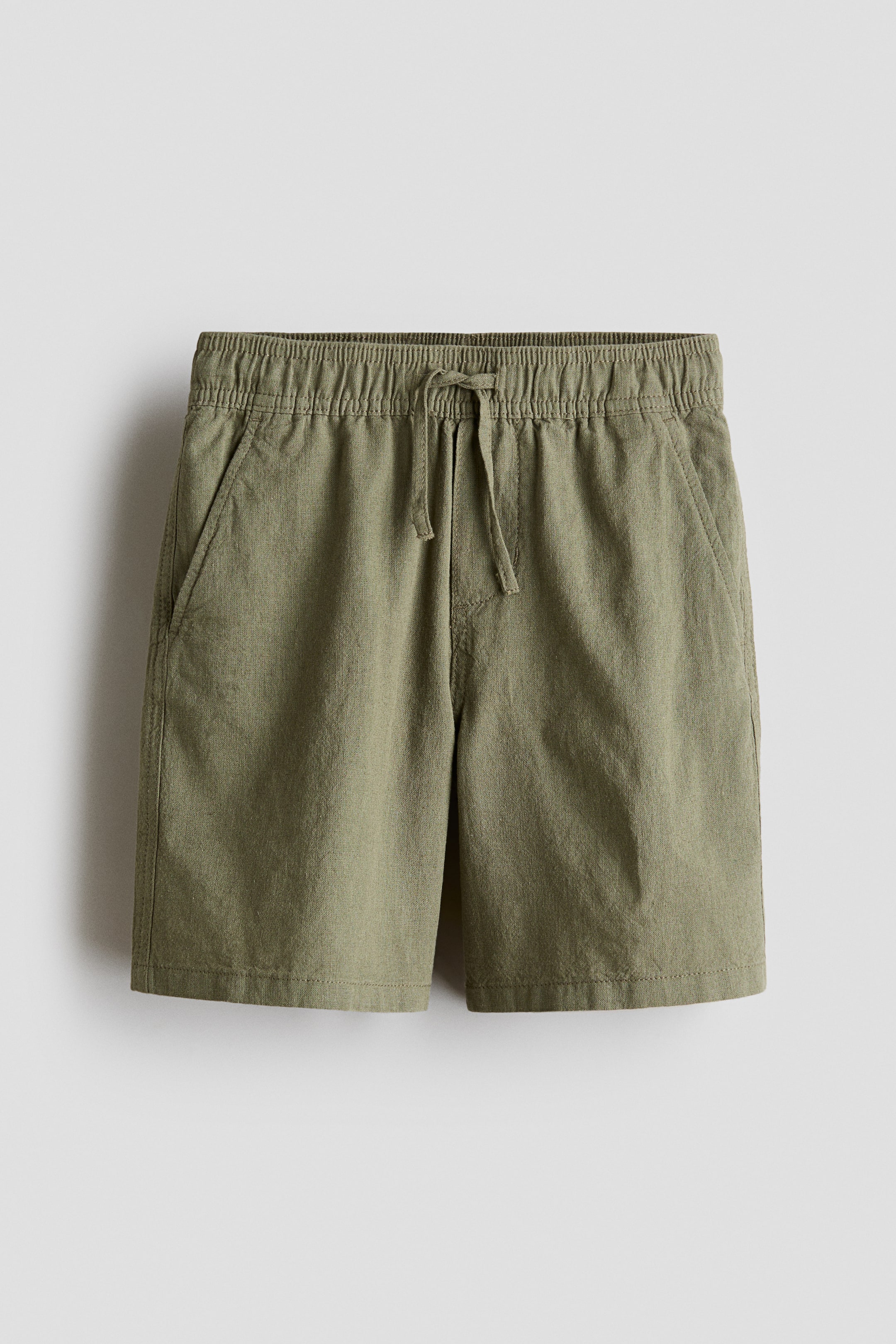Vis større bilde: Oliven grønne shorts med en teksturert bomull- og linvev. De har elastisk snøring i midjen, en sydd falsk gylf, og diagonale frontlommer.