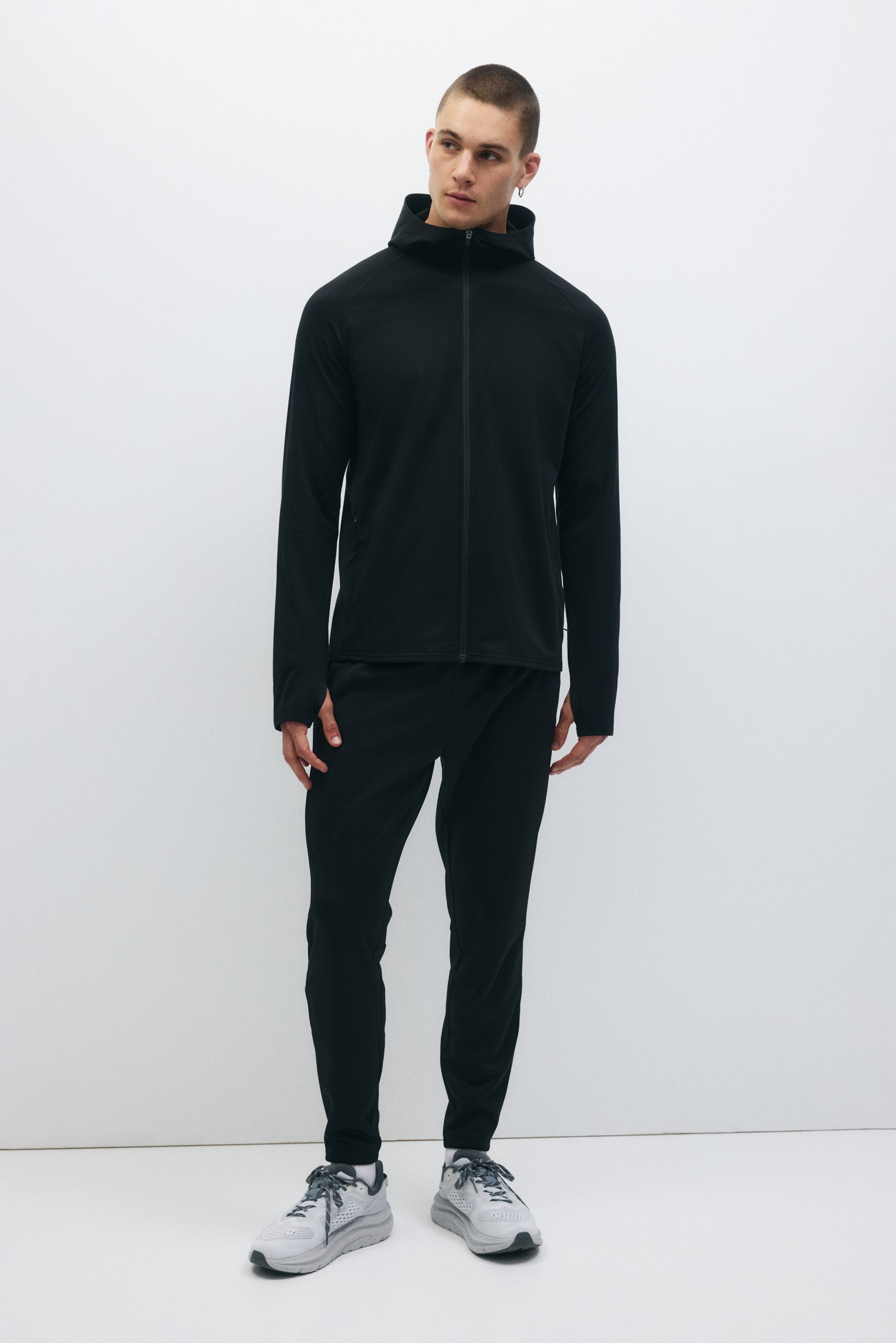 View larger image: Presenting a black tracksuit, comprising a hooded jacket with a full-zip fastening, a high neck, raglan sleeves with thumbholes, and a zipped side pocket. The coordinating joggers feature a tapered fit.