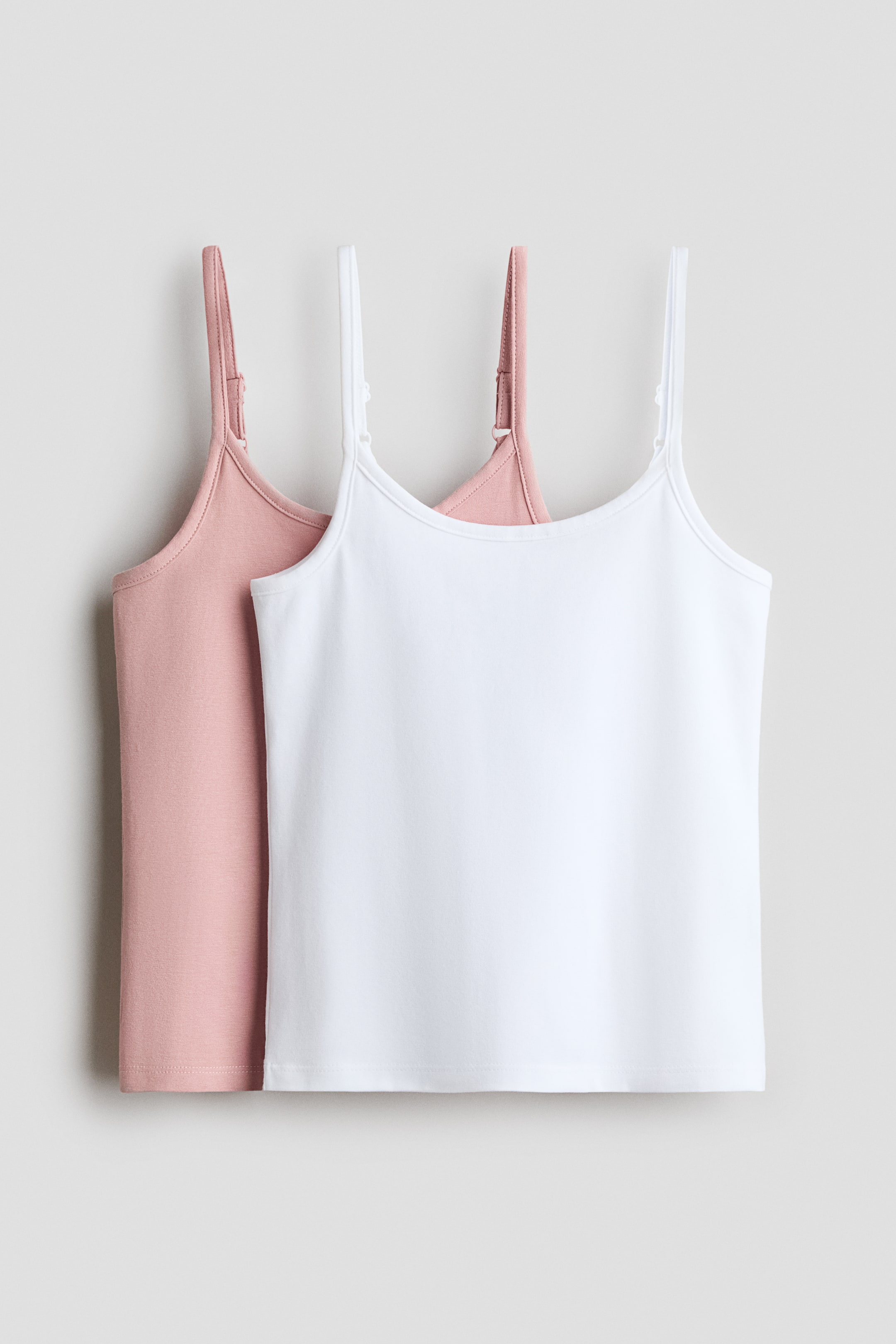 View larger image: Two cotton jersey camisoles, one in white and one in dusty pink, are hanging front-facing. The white cami overlaps the pink cami, with both featuring scoop necklines and thin, adjustable spaghetti shoulder straps.