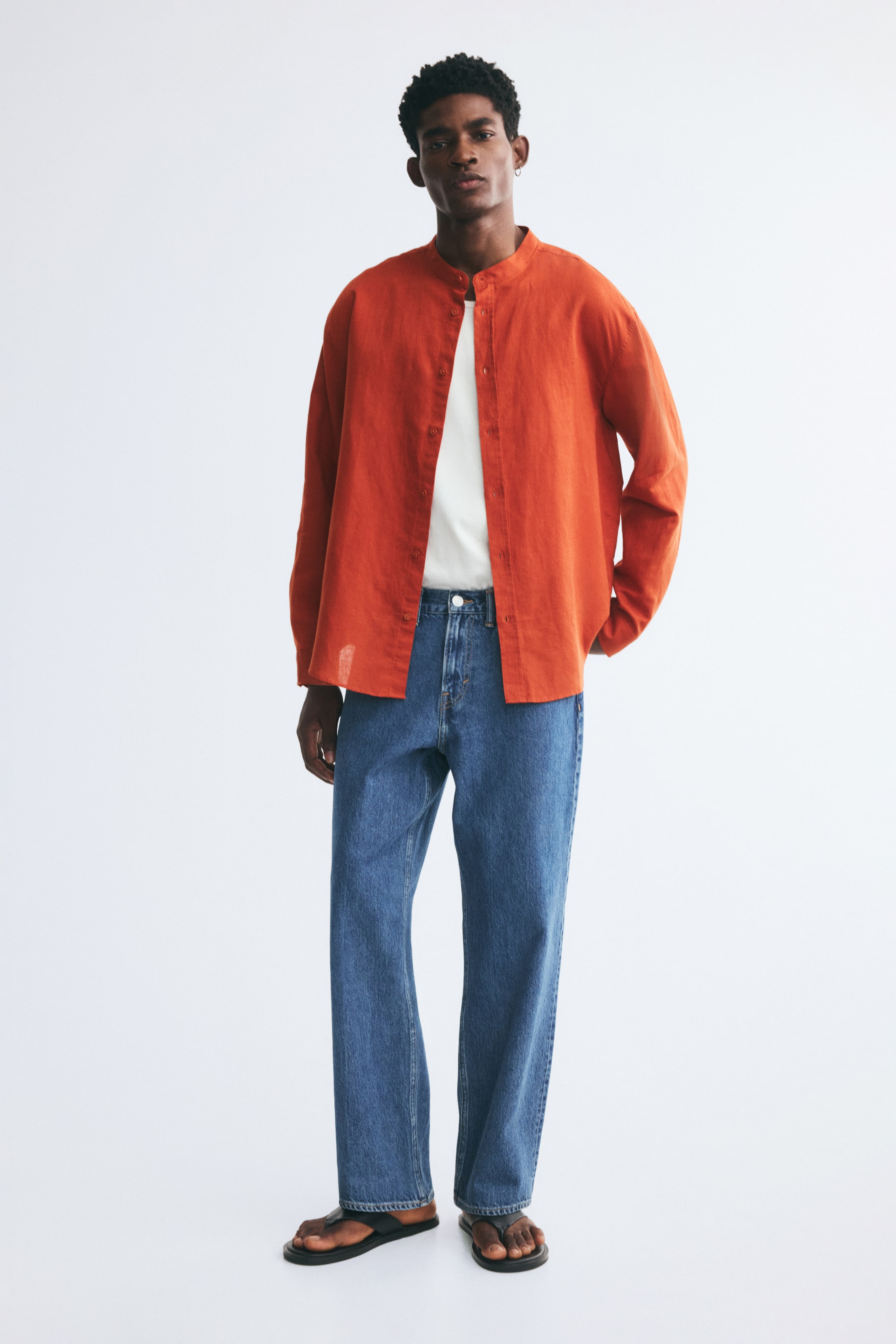 View larger image: An orange, long-sleeved shirt in a textured linen and cotton blend is worn open by the model over a white T-shirt and blue jeans. The relaxed-fit shirt features a band collar, a button-up front, and a rounded hem.