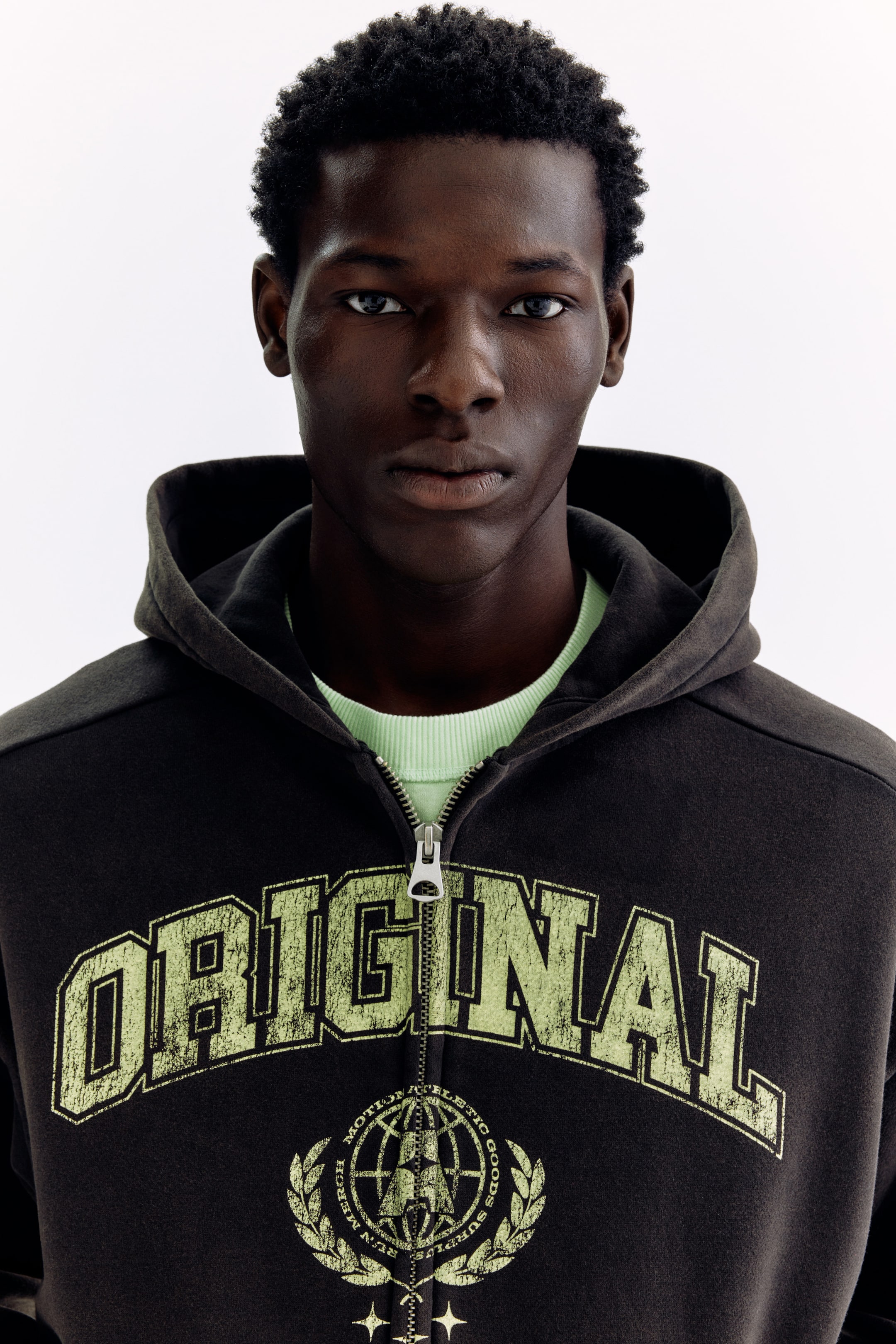 View larger image: "呢件深灰色全拉鏈帽衫，胸口上印有淺綠色做舊效果嘅『ORIGINAL』字樣，下面仲有一個圓形標誌。部分拉開嘅帽衫底下，仲可以見到一件淺綠色嘅圓領衫。"