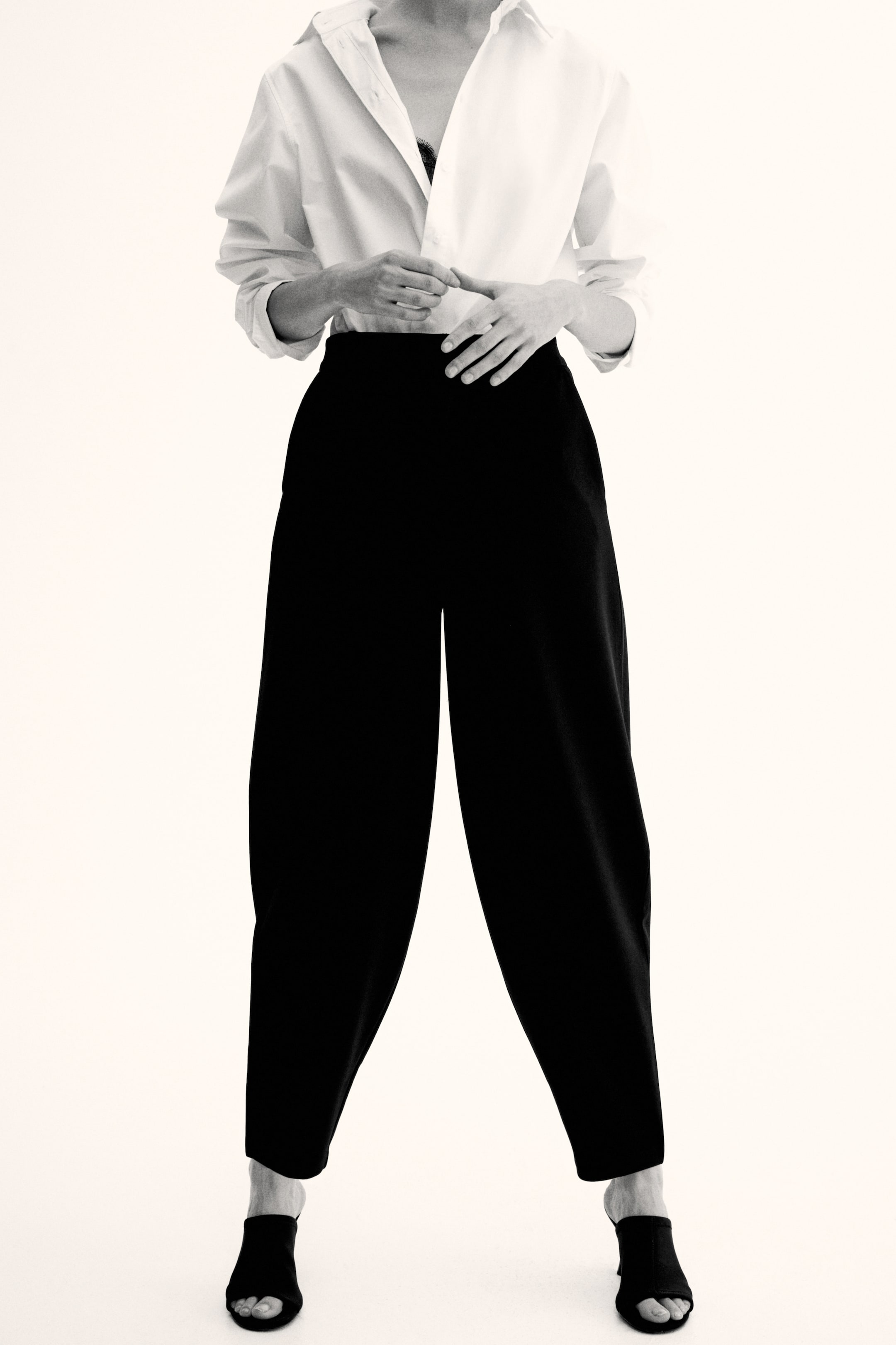 View larger image: "Black trousers feature a high-waisted design with a voluminous, tapered silhouette, clearly visible from the front and extending down to the ankles."
