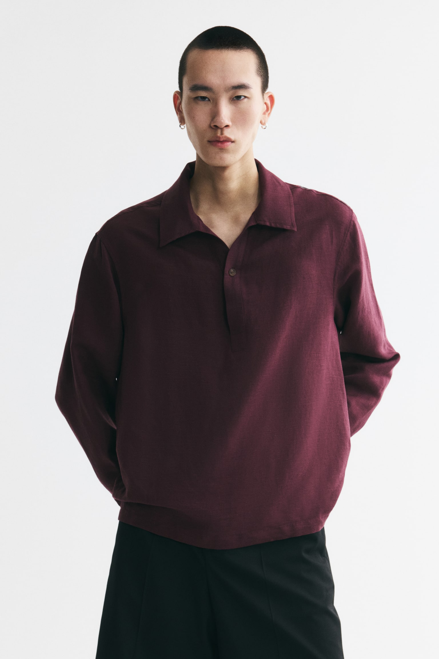 A maroon long-sleeved shirt menampilkan kolar lebar dan plaket butang separa dengan satu butang kelihatan. Ia mempunyai fabrik bertekstur dan lengan panjang yang polos. - 1