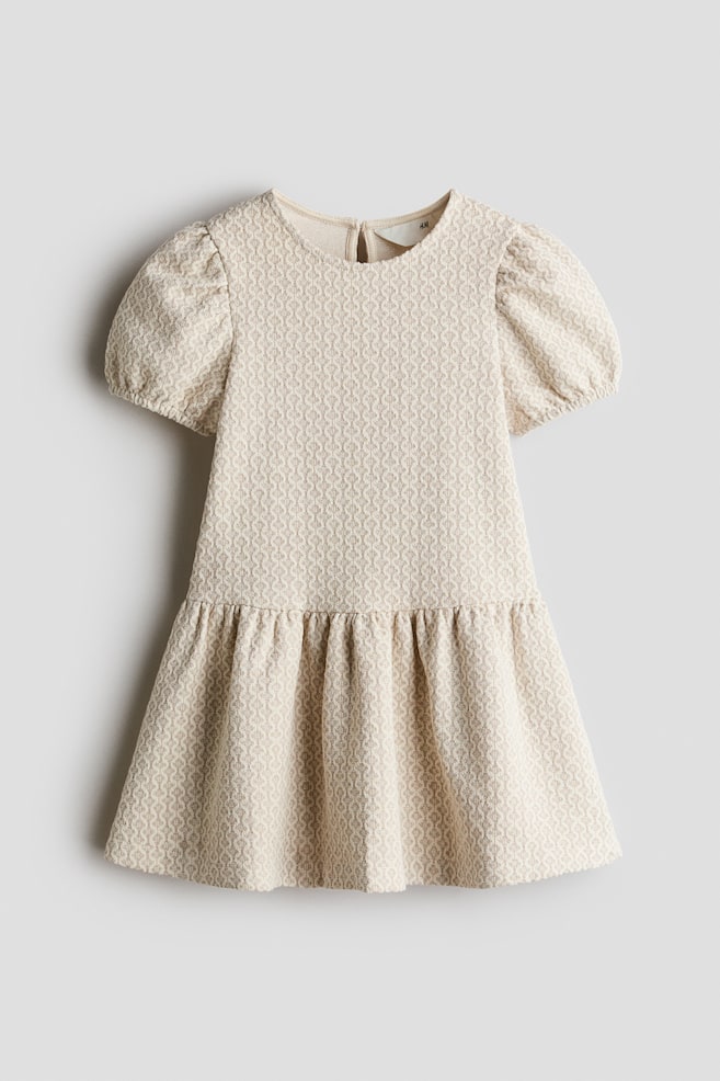 A child's dress in a beige and cream textured knit is featuring a round neckline, short puff sleeves with elasticized cuffs, and a gathered skirt. This front view showcases the structured bodice and the flared, gathered design of the skirt. - 1