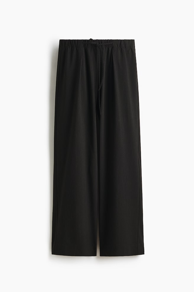 Loose-fit pull-on trousers in black woven fabric are presenting their FRONT, featuring subtle vertical pinstripes, an elasticated drawstring waist, and straight legs with pleats at the front. - 1