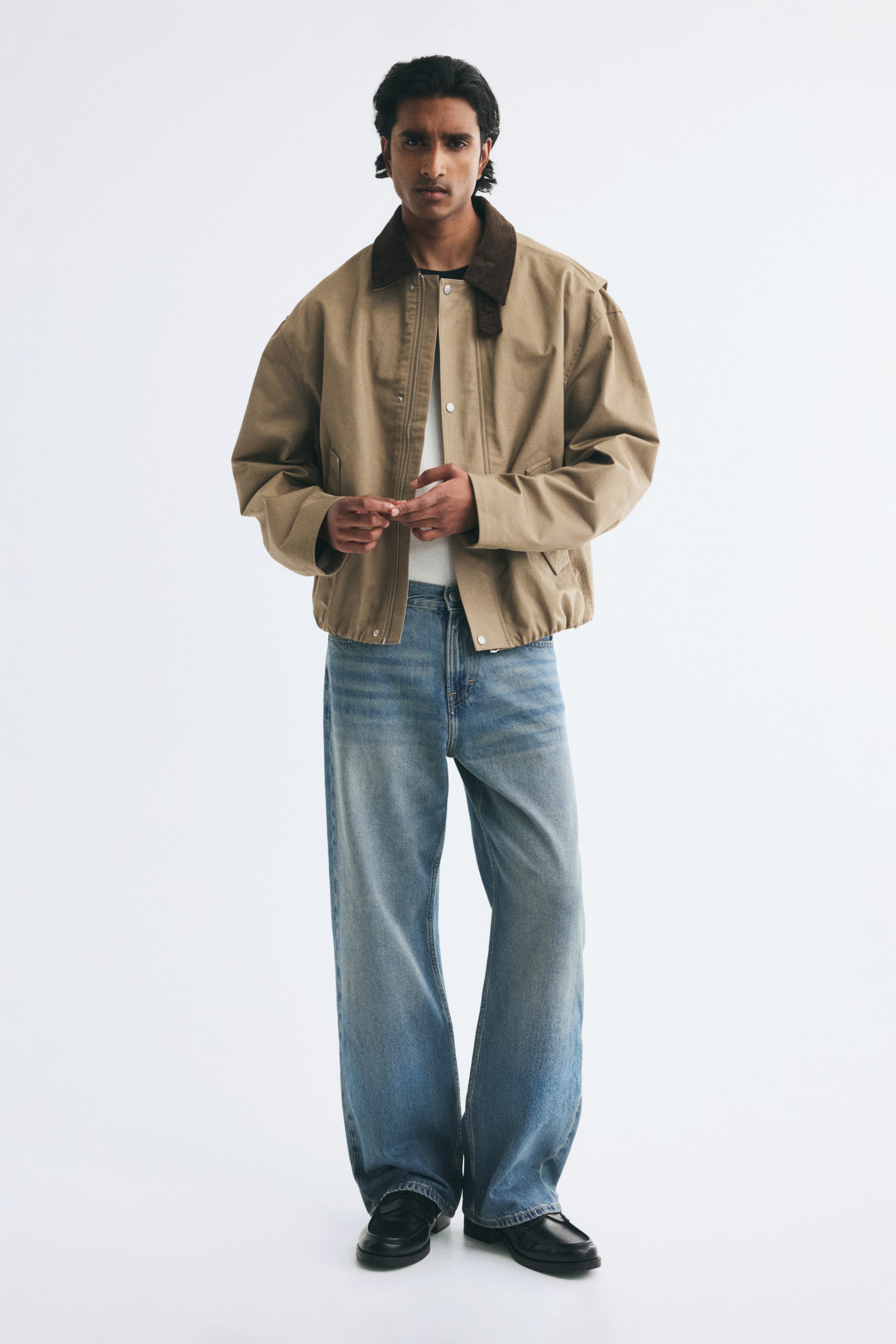 View larger image: Blue denim jeans featuring a loose, straight-leg fit and a light wash are being worn by the model. The jeans are styled with a tucked-in white T-shirt, a tan jacket with a brown collar, and black leather shoes.